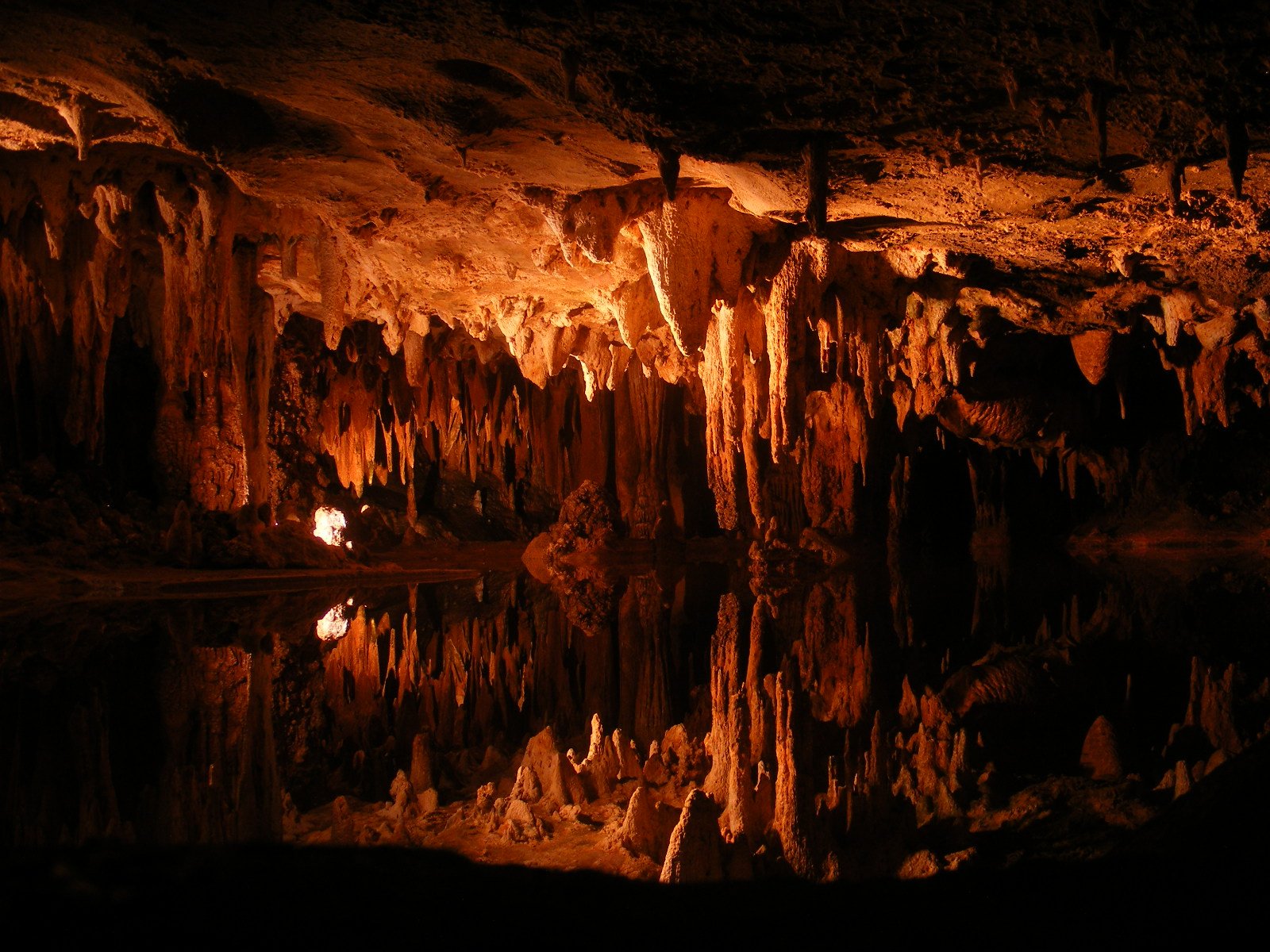 A breathtaking view of an illuminated cave with stalactites and stalagmites reflected in the still water below