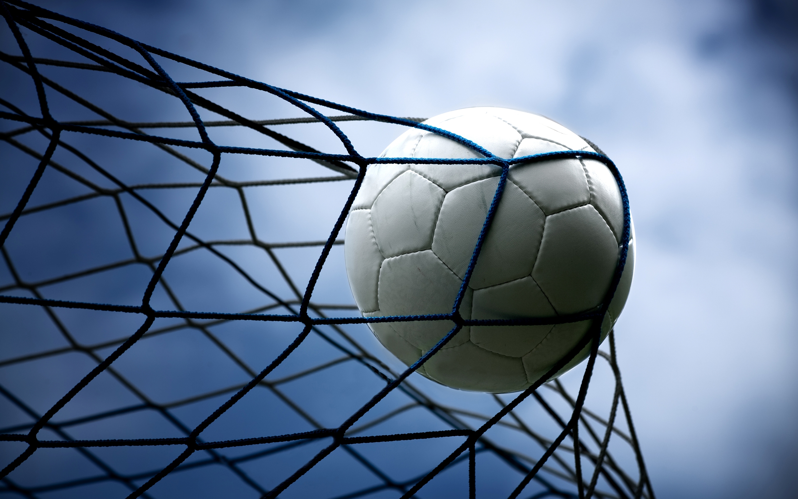 A white soccer ball hitting the back of a net against a dramatic blue sky, celebrating a goal in an intense match