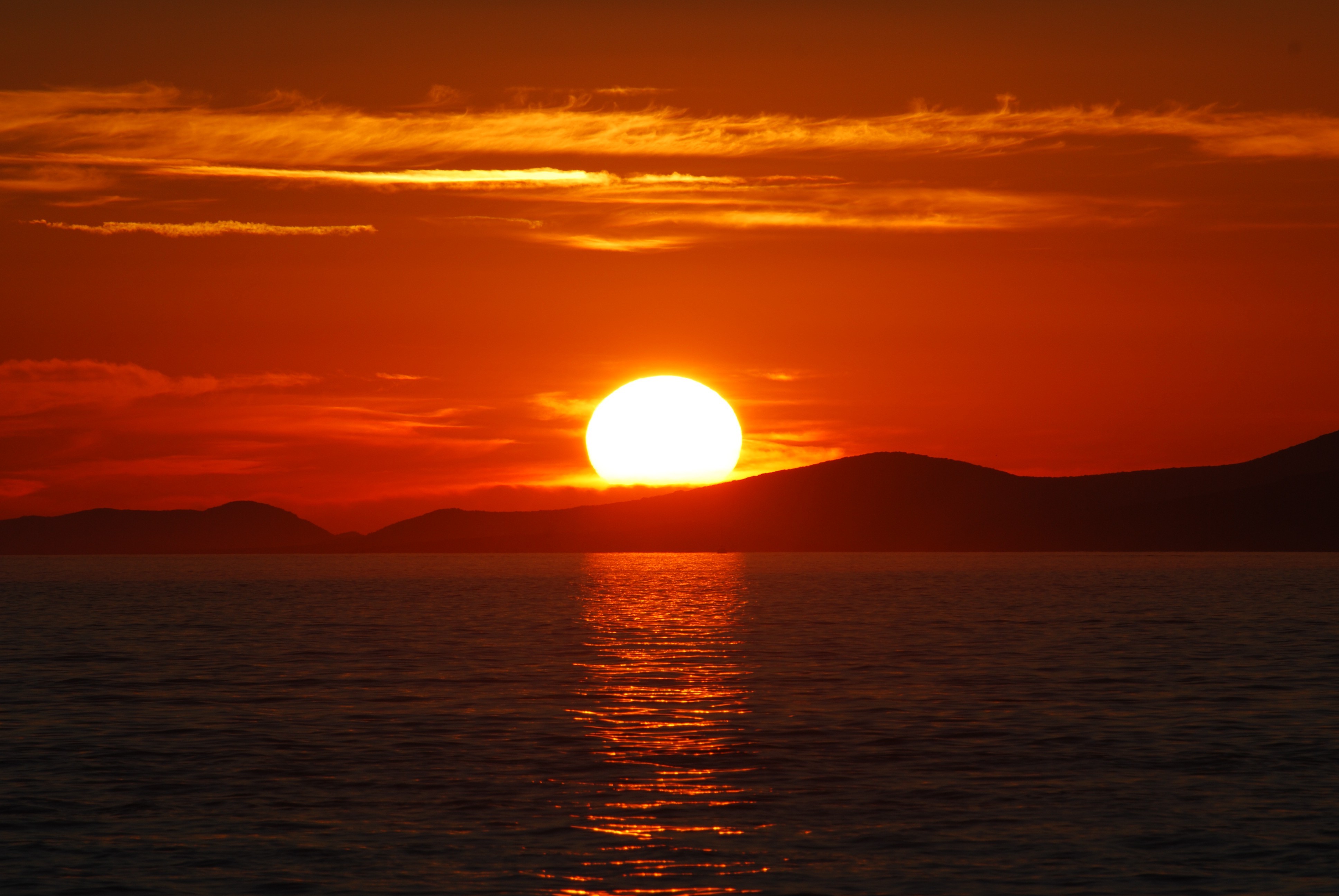 A breathtaking sunset over a tranquil ocean with the sun dipping below the horizon, casting a warm orange glow on the sky and water