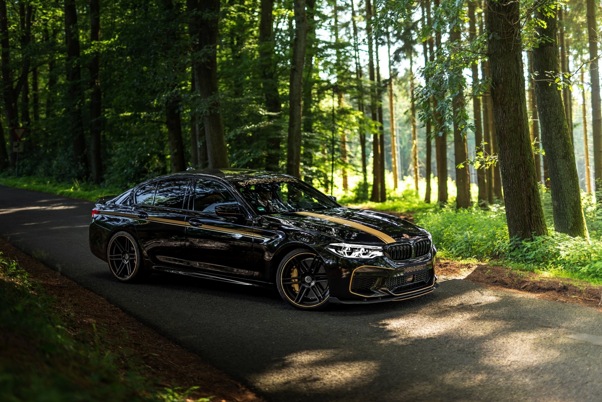Black BMW M5 with Gold Accents Driving Through Forest Road