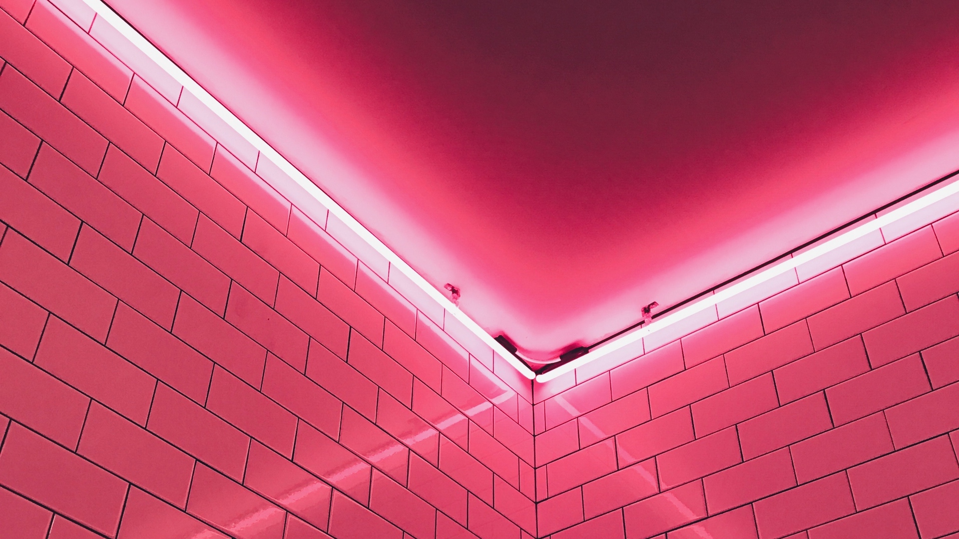 Vibrant pink neon light illuminating a corner of a room with pink subway tiles, creating a modern and stylish aesthetic