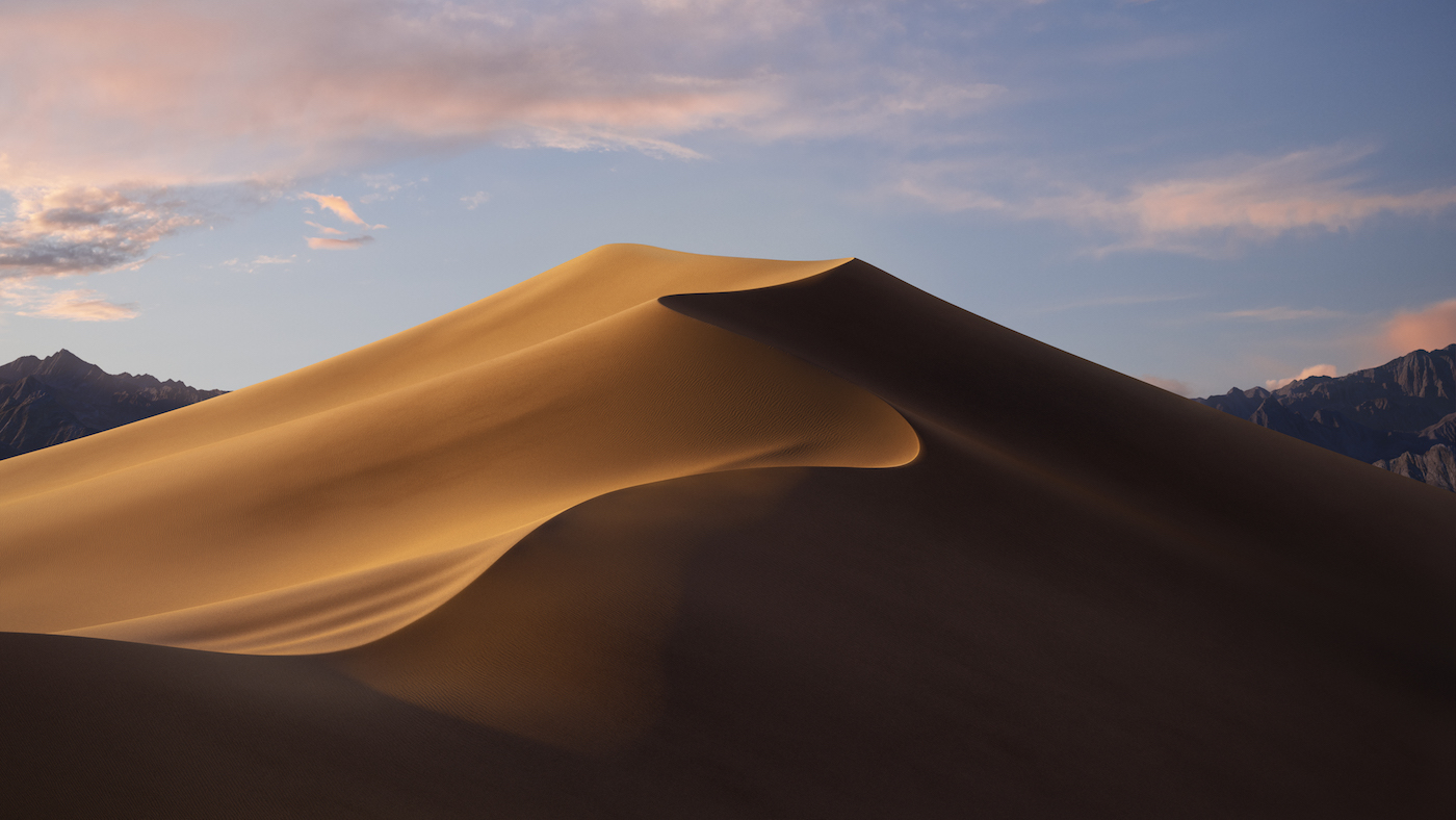 Mesquite Flat Sand Dunes in Death Valley National Park at sunset. The dunes are illuminated by the setting sun, creating a warm glow on the sand. Mountains rise in the background under a soft sky