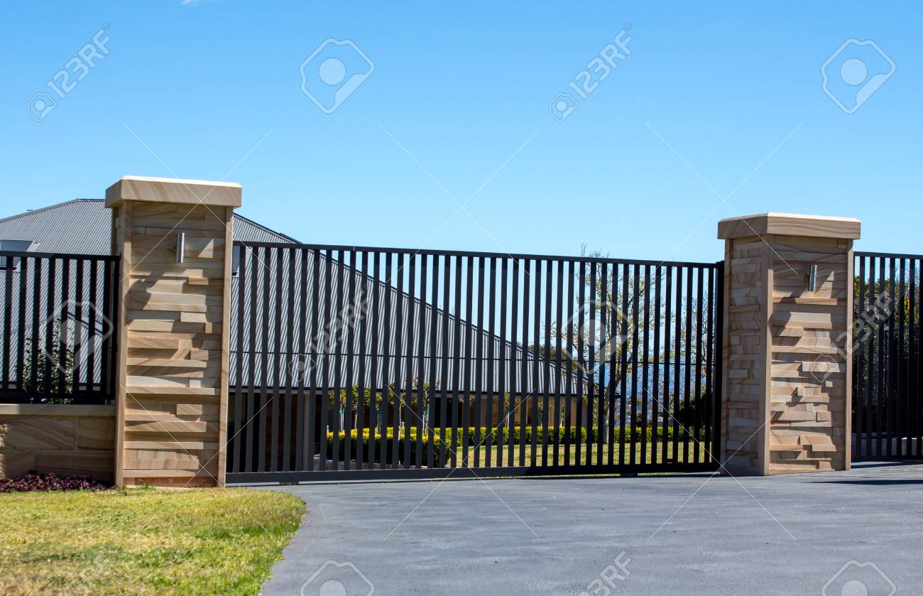 Black Metal Driveway Entrance Gates Set In Sandstone Brick Fence
