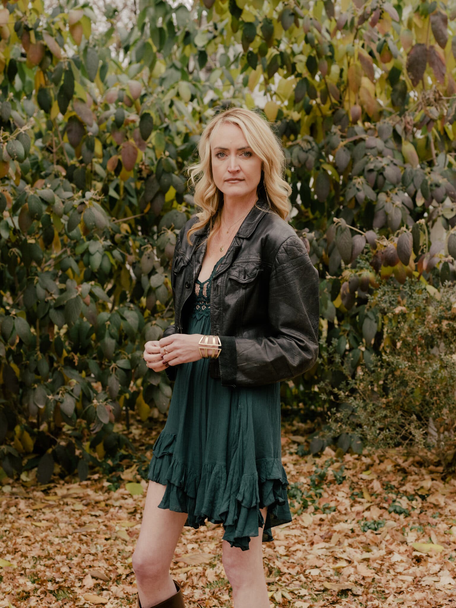 Emily Armstrong stands in front of a leafy bush, wearing a green dress and black leather jacket