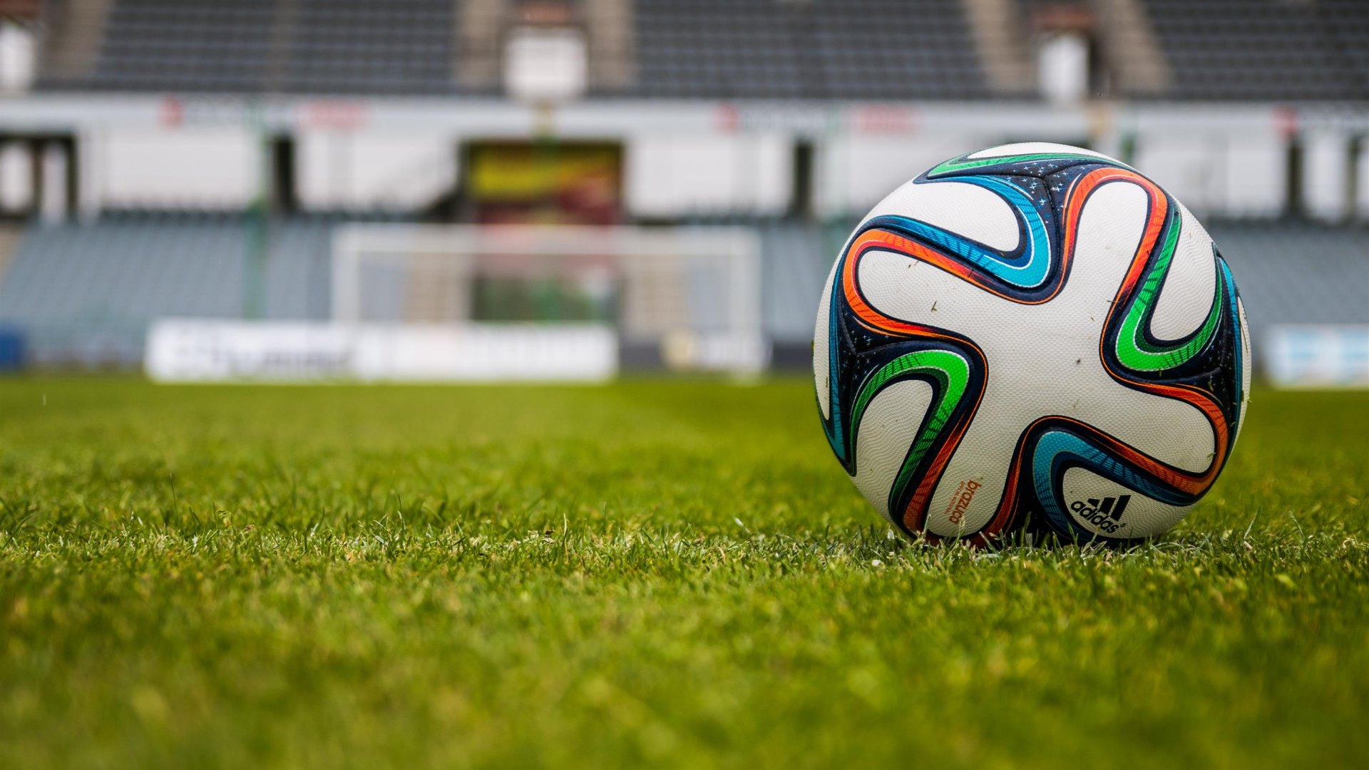 A vibrant soccer ball sits on a lush green field in a stadium, ready for the next game