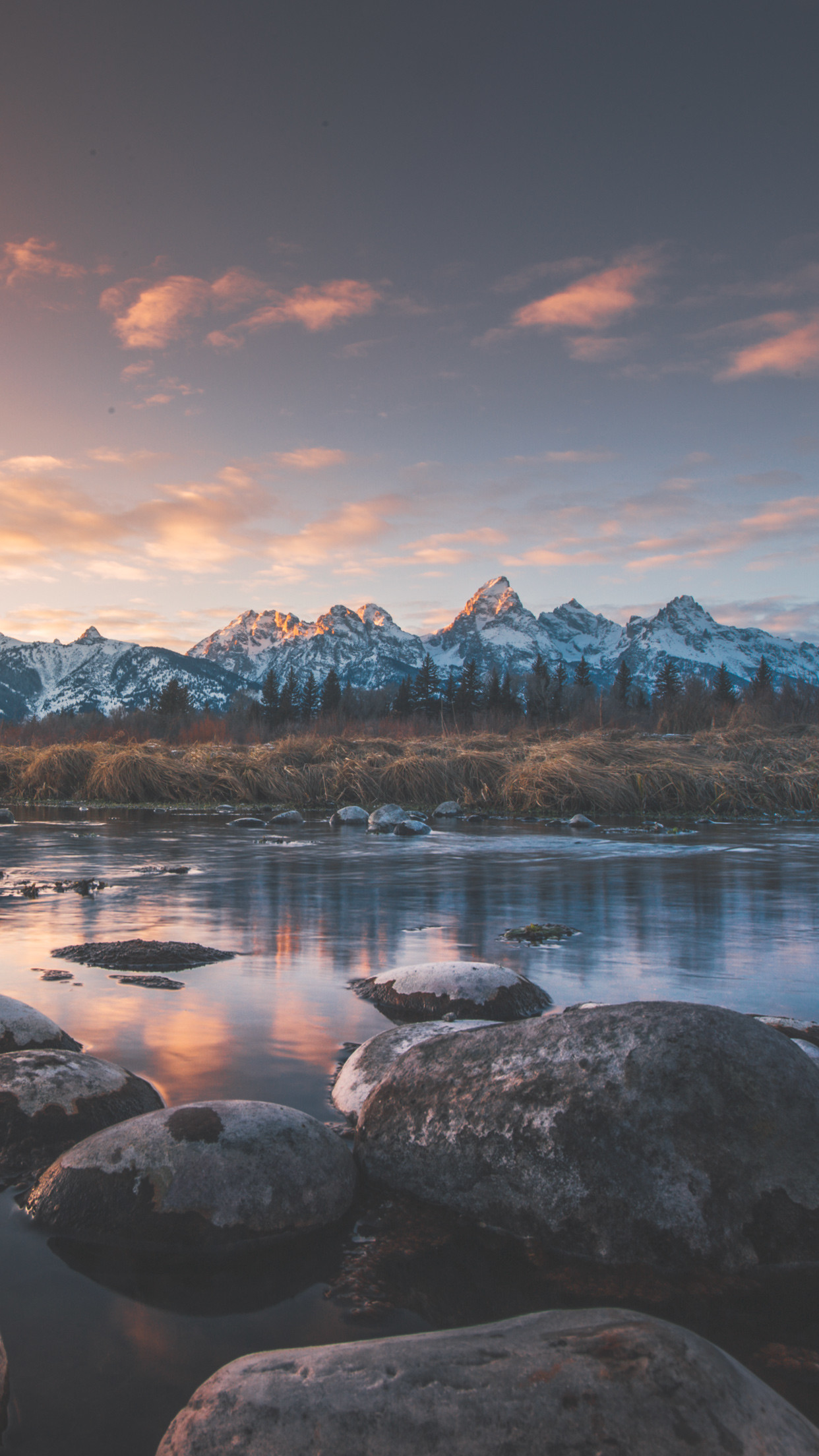 Sunrise over the Grand Teton mountain range with a calm river in the foreground