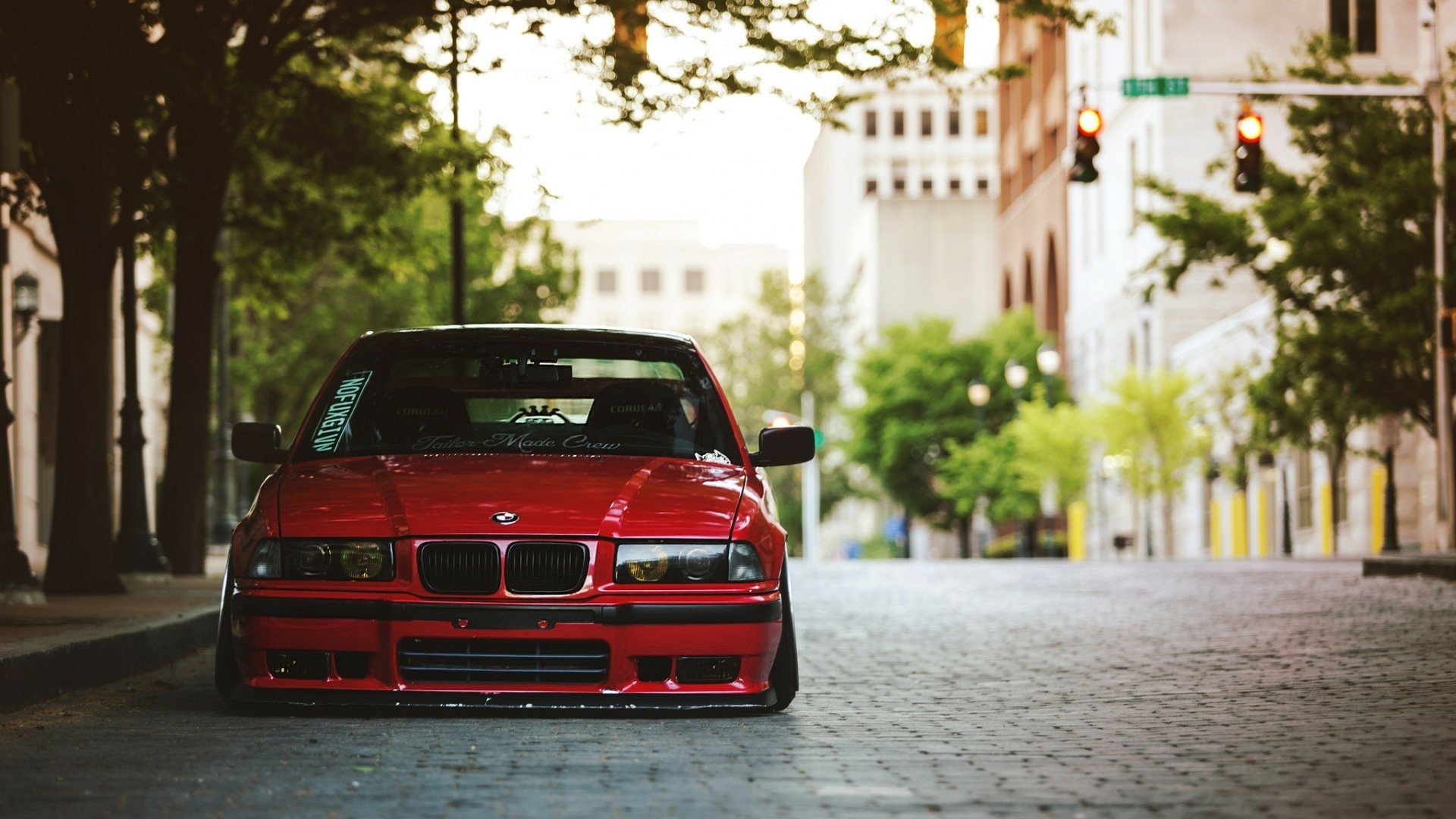 Red BMW E36 parked on a cobblestone street