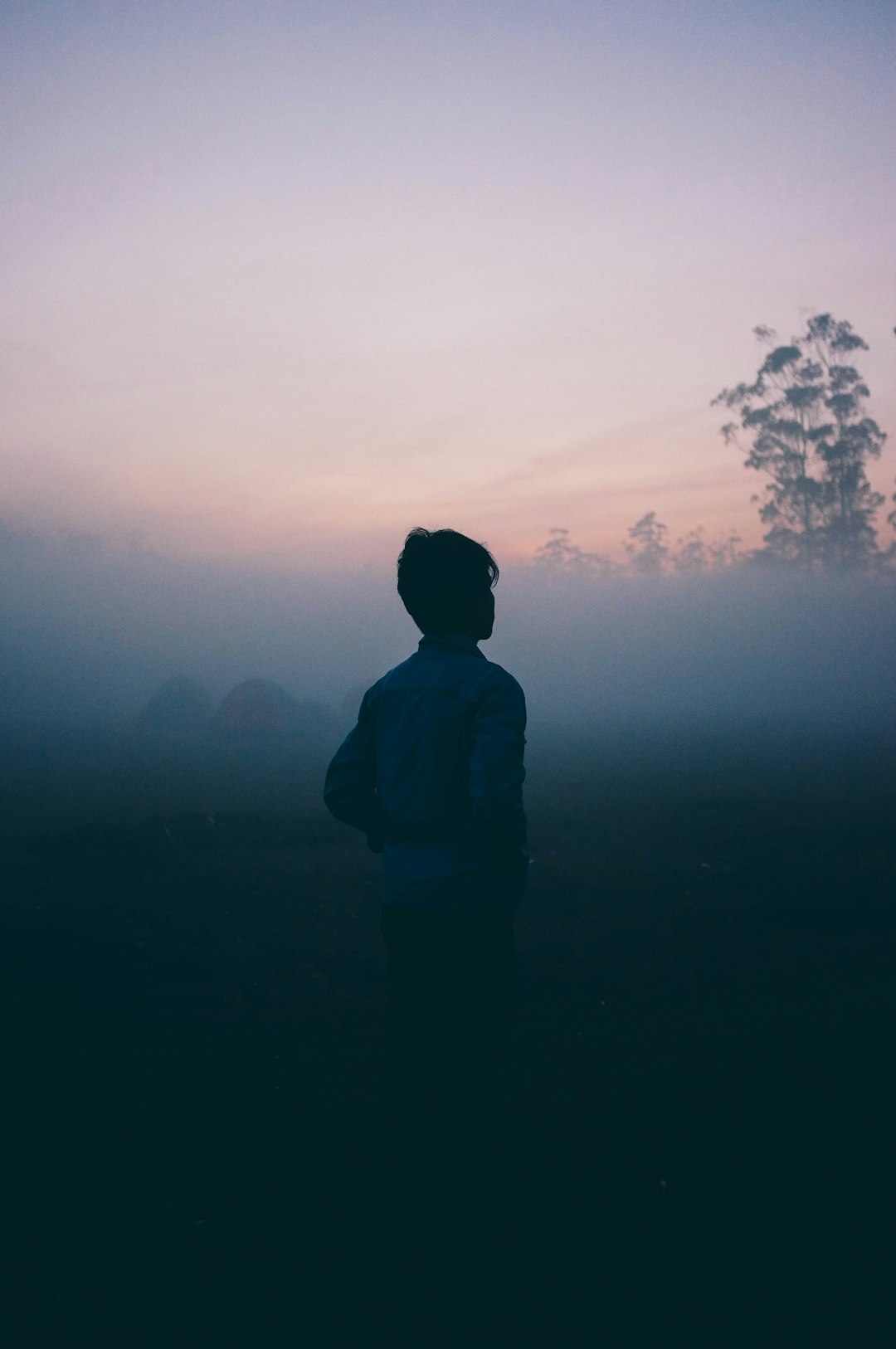Silhouette of person standing against misty sunrise, evoking feelings of solitude and contemplation