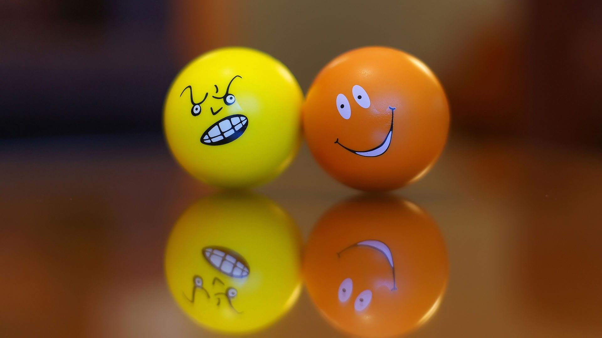 Two emoji balls: One angry yellow and one happy orange, reflected on a surface