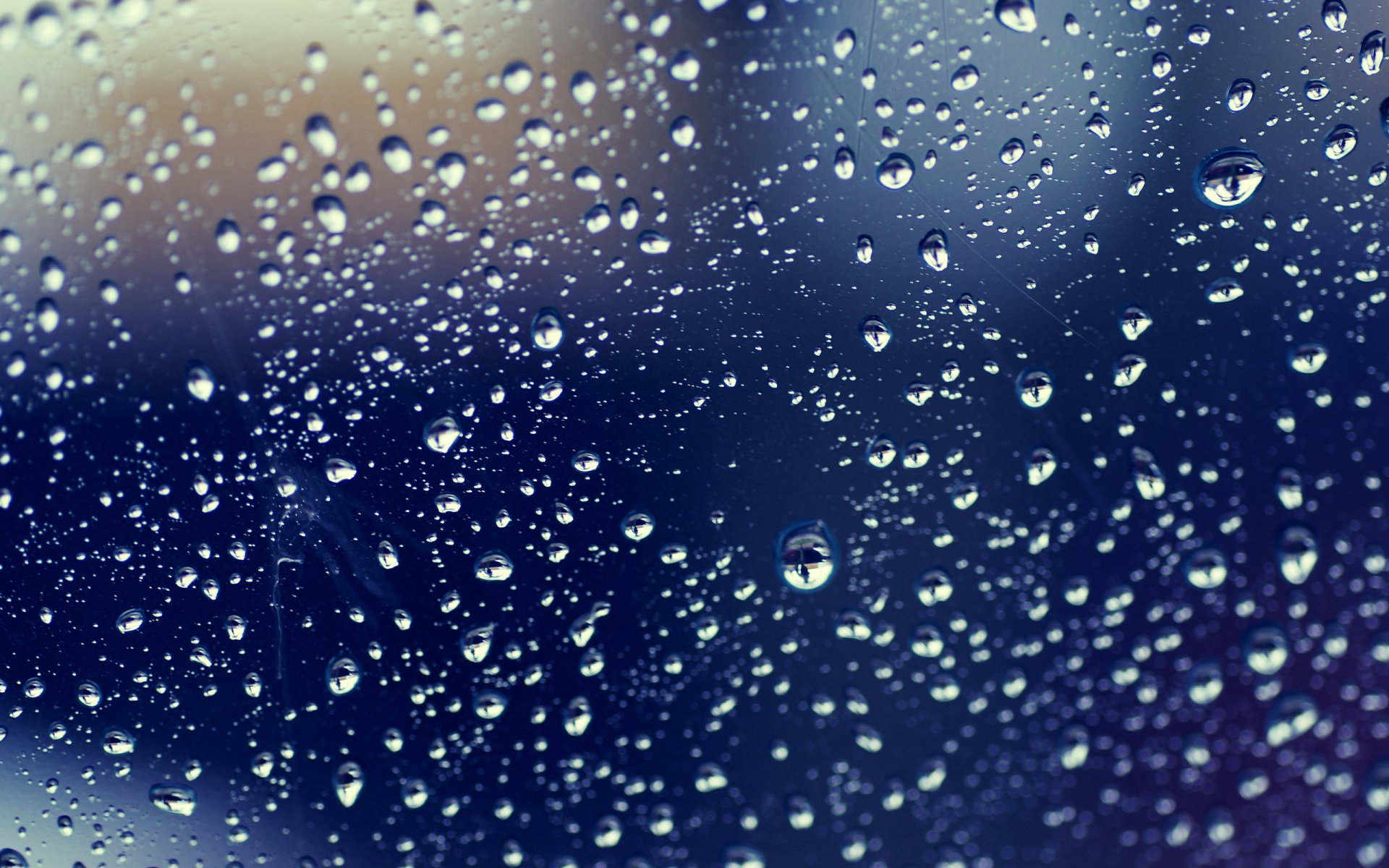 Close-up of raindrops on a window, creating a textured, abstract pattern against a blurred background