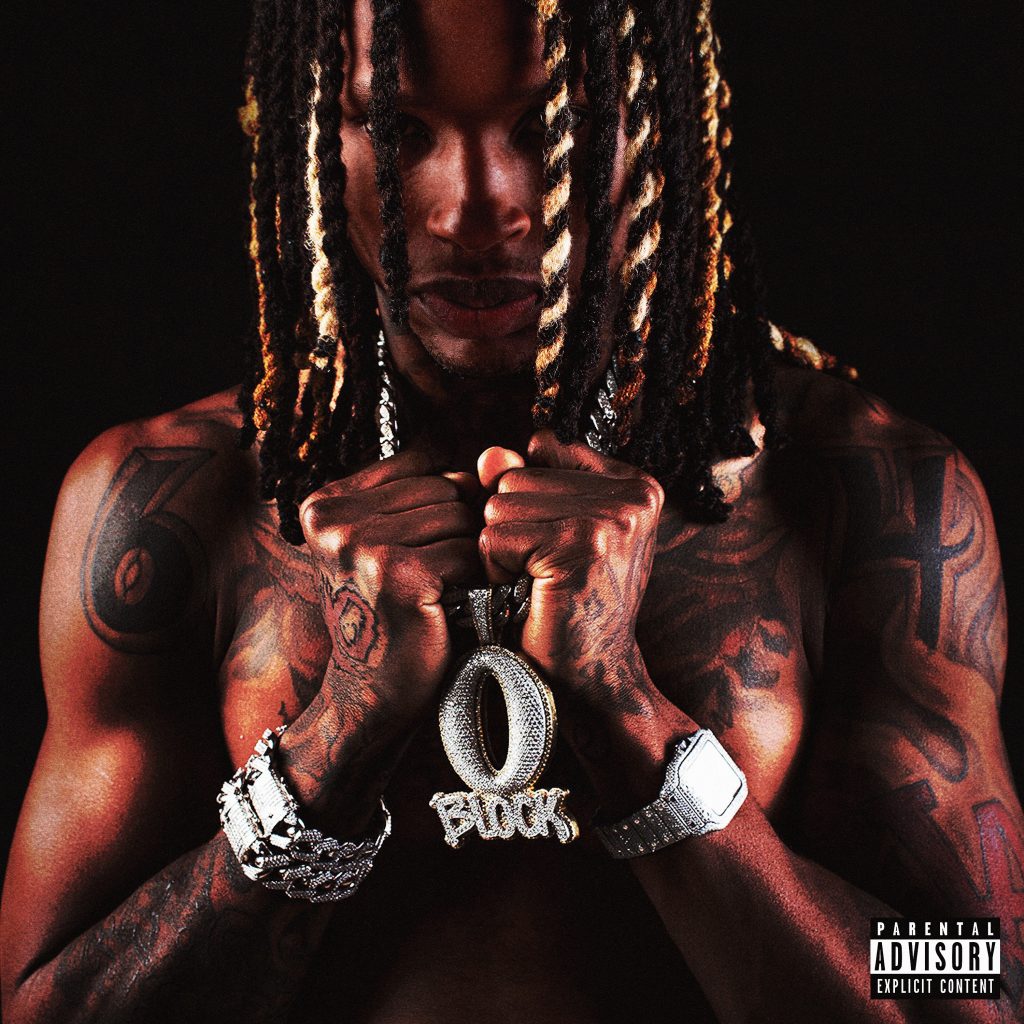 A rapper with dreadlocks and tattoos holding a large diamond pendant