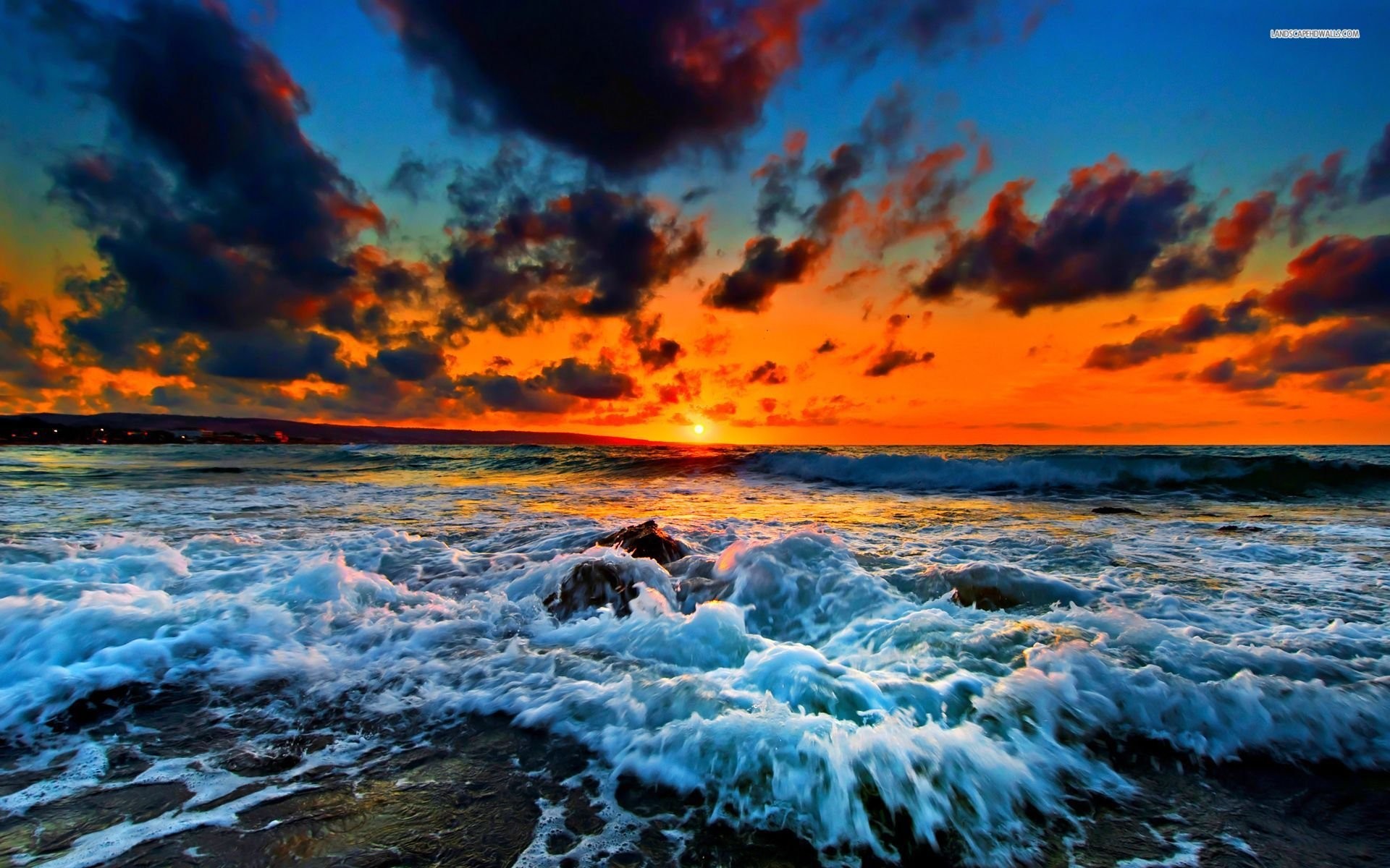 Sunset over a vibrant ocean with crashing waves on a rocky beach