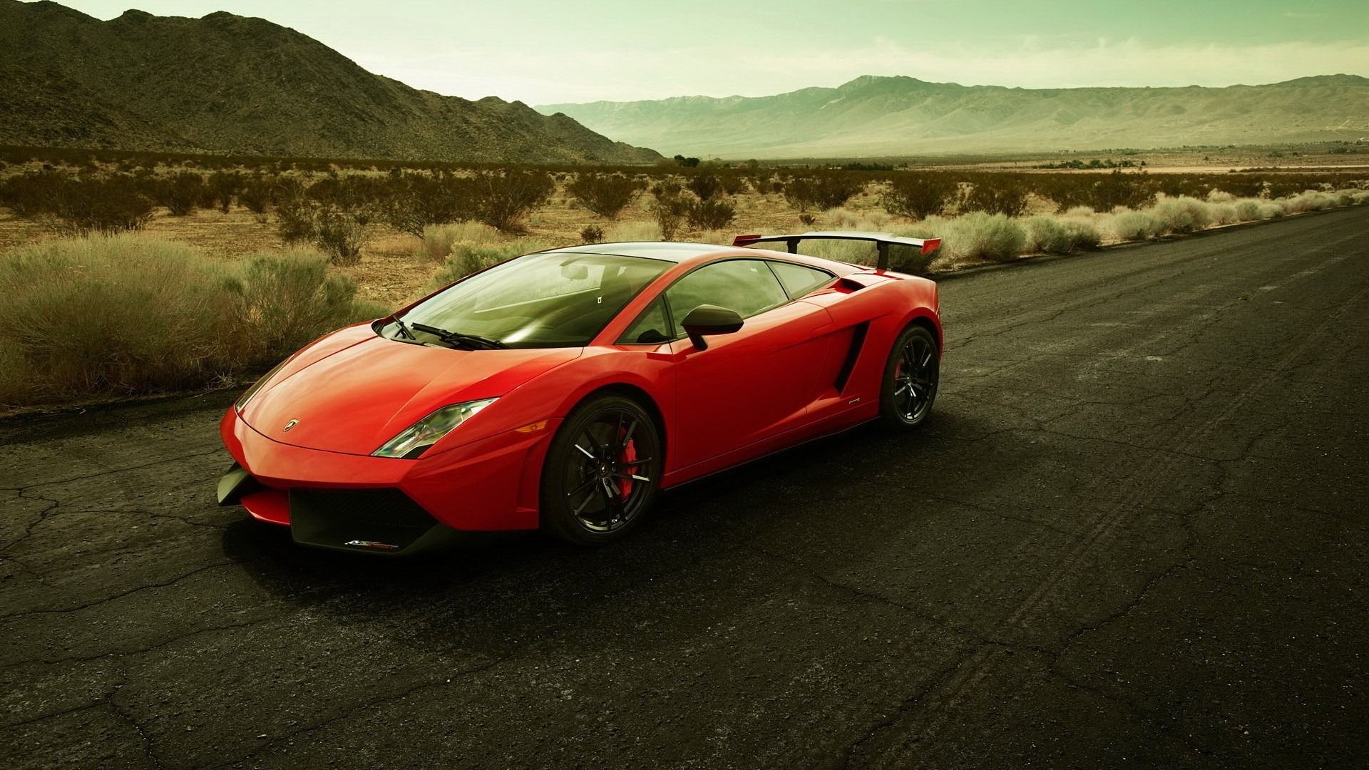A vibrant red Lamborghini Gallardo parked on a desert road, with mountains in the background