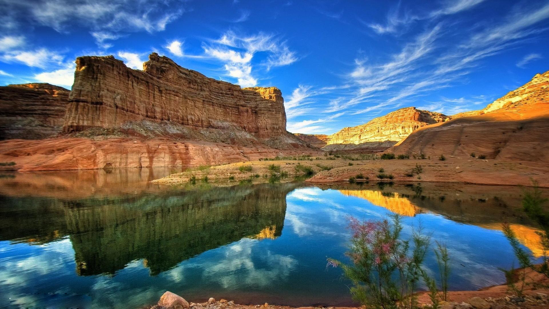 Stunning desert landscape with red rock formations reflected in a calm river under a vibrant blue sky