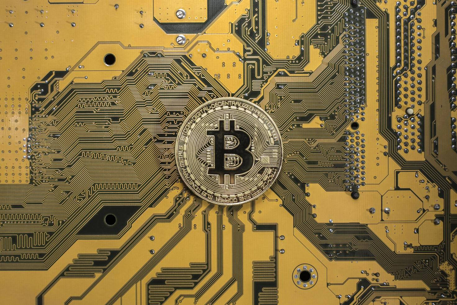 A gold Bitcoin sits atop a golden computer circuit board, symbolizing the digital and technological nature of cryptocurrency