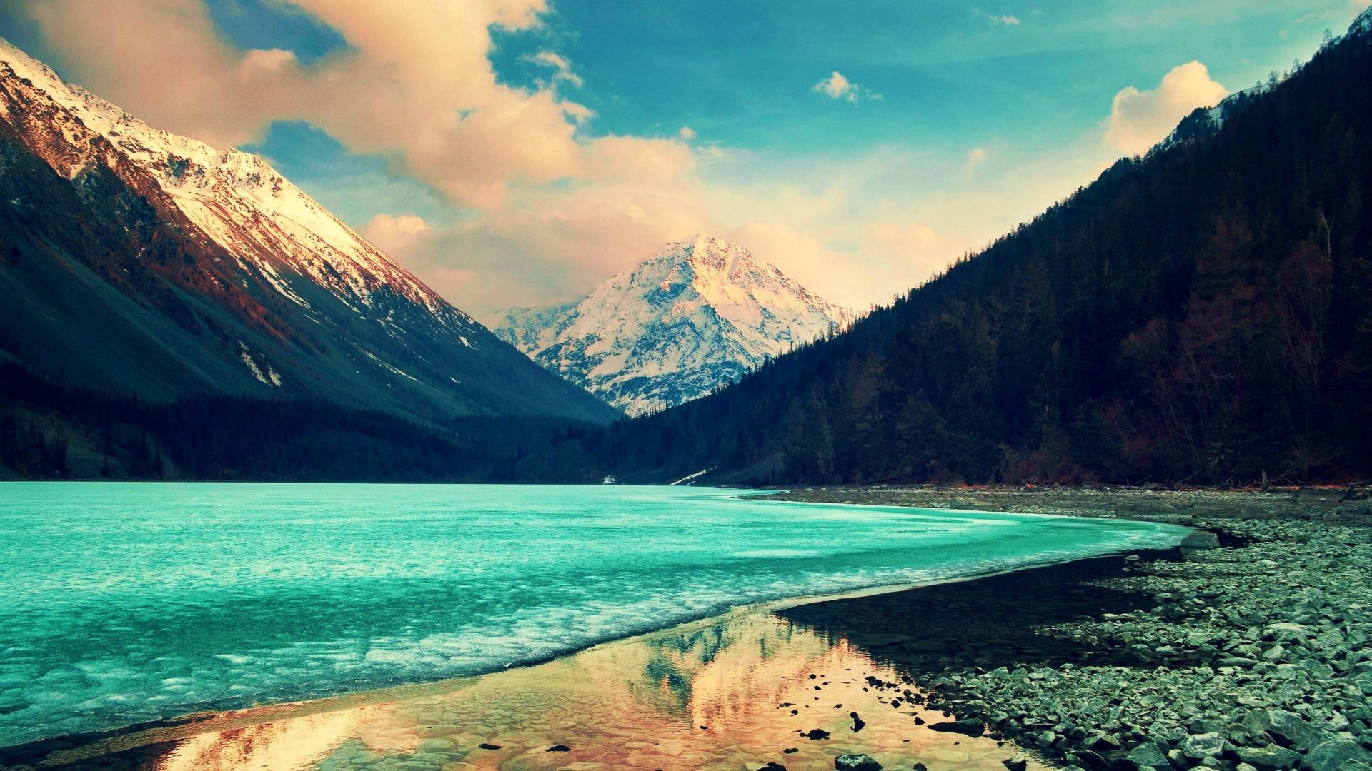 Stunning 4K background image of a turquoise lake nestled amidst snow-capped mountains and a dense forest