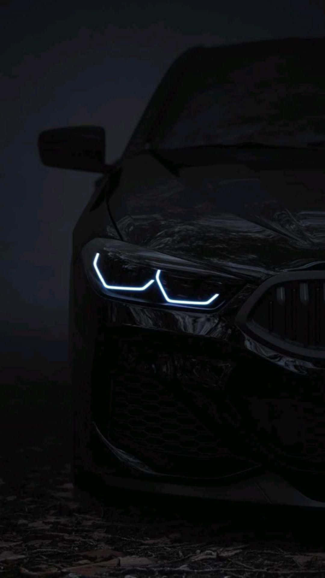 A sleek, black BMW M5 with its iconic headlights illuminated, parked in a dimly lit environment