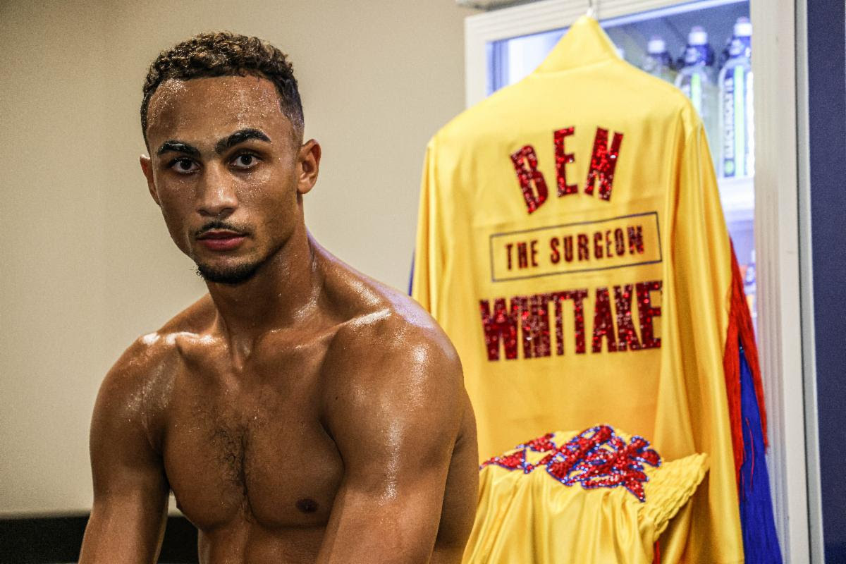 Shirtless Benjamin Whittaker sitting with his boxing robe in the background. The robe says 