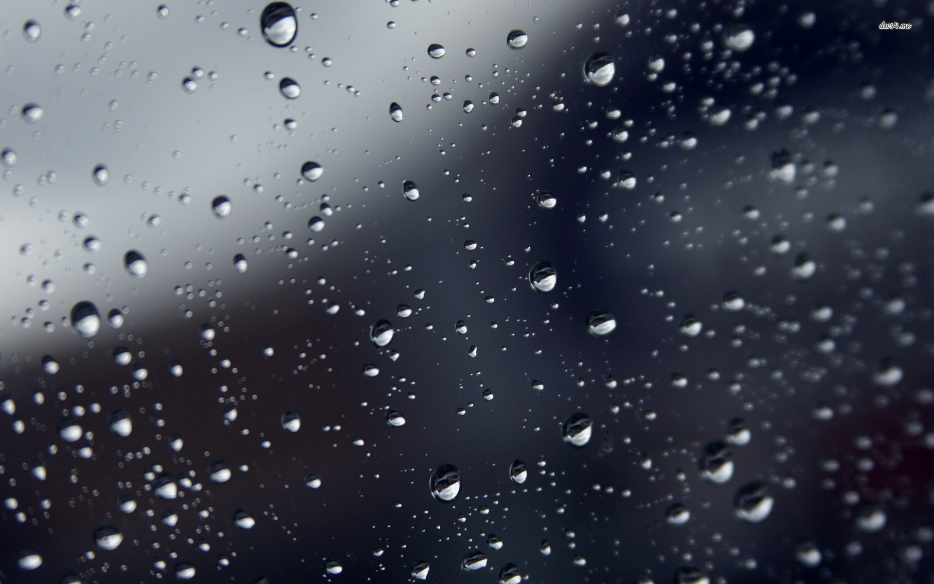 Close-up of raindrops on a window pane against a blurred dark background, evoking a melancholic mood