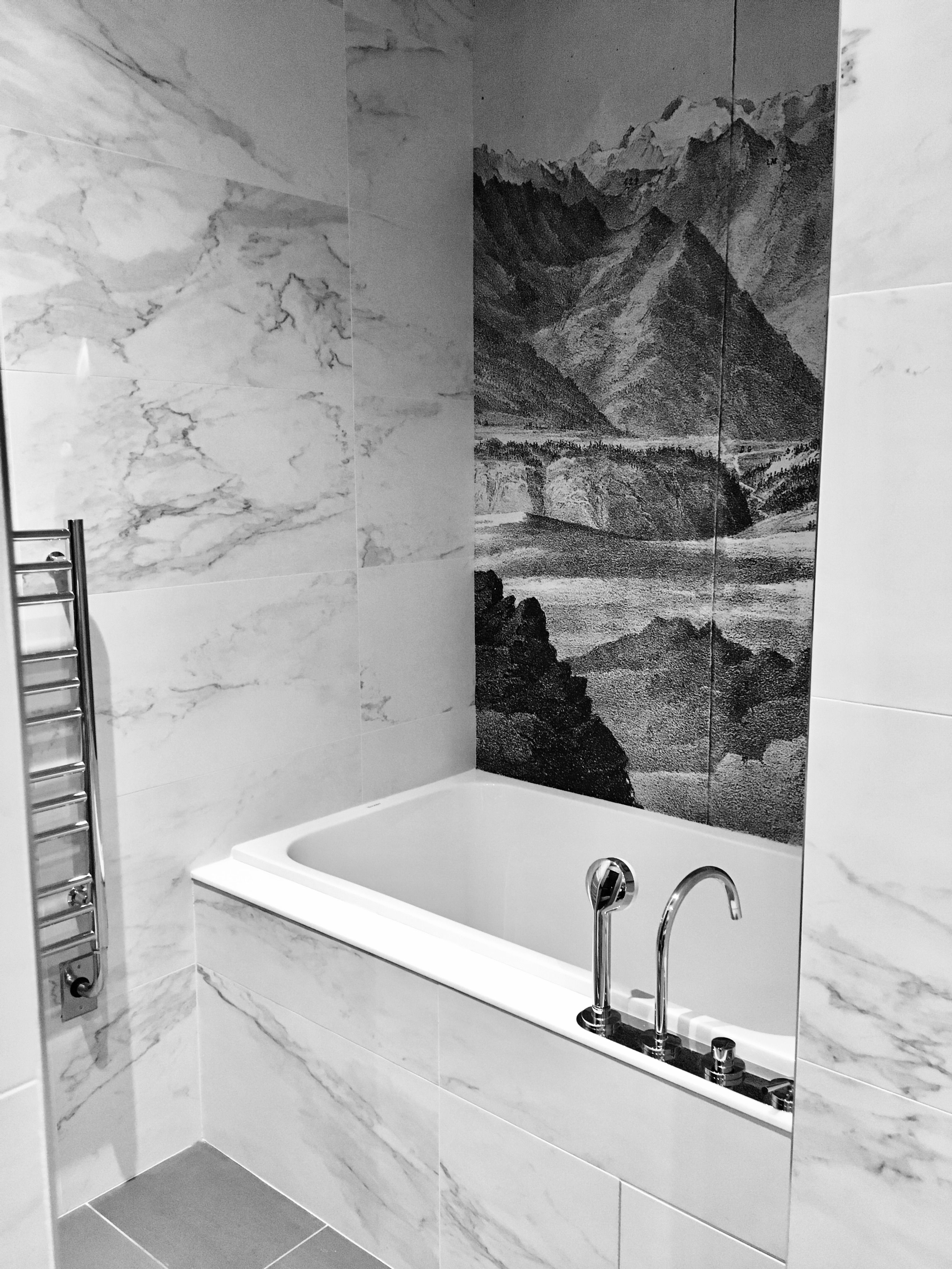A White Bath Tub Sitting Inside Of Bathroom Next To Painting On The Wallpaper