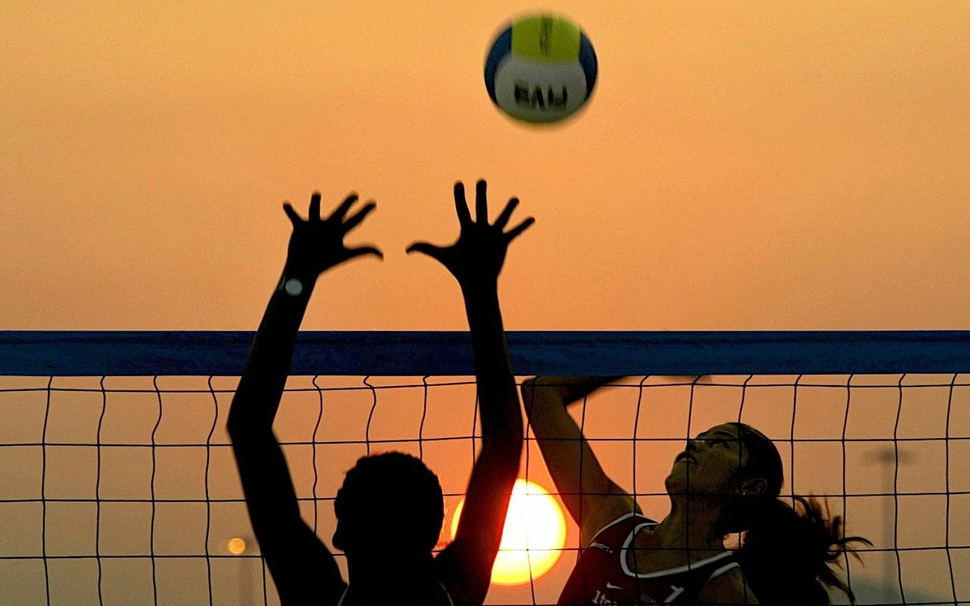 Silhouetted volleyball players against a vibrant sunset backdrop during a beach volleyball match