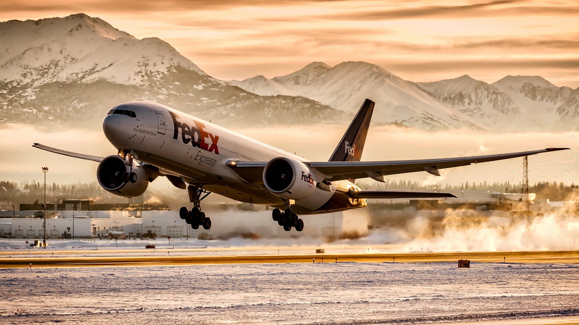 FedEx Boeing 777 taking off from a snowy runway against a backdrop of snow-capped mountains