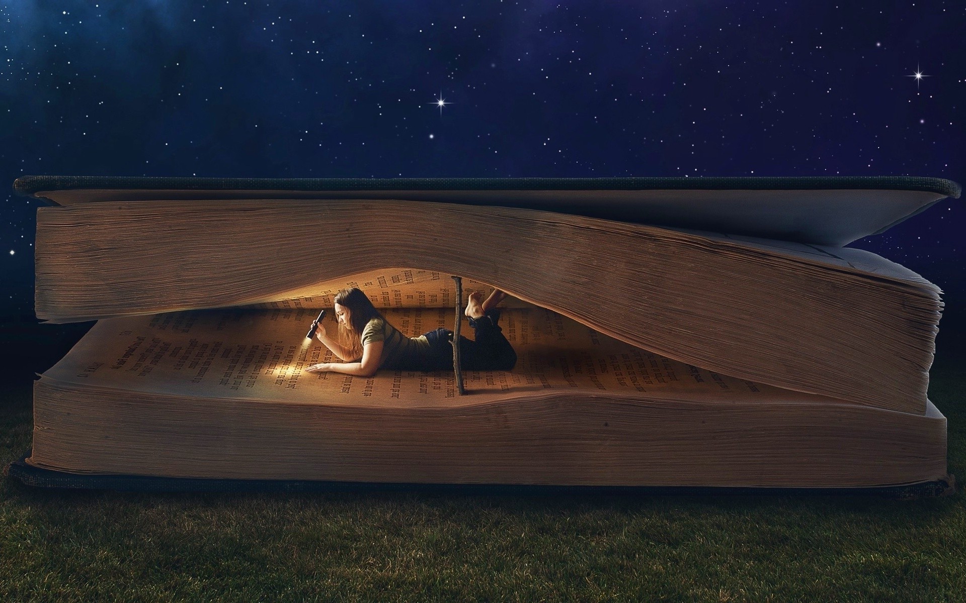 A woman lies on her stomach inside a giant, open book, using a flashlight to read under the starry night sky. This surreal image evokes the magic and wonder of reading