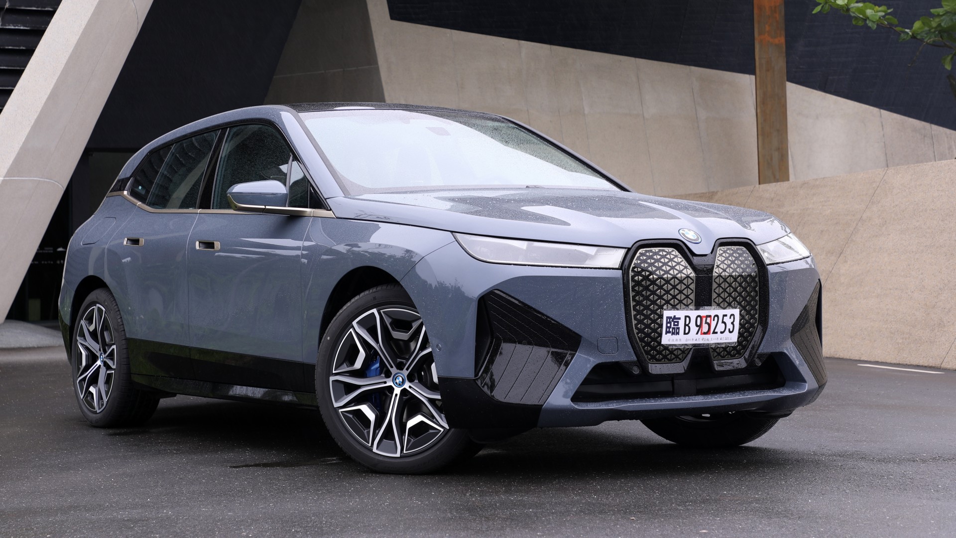 A sleek, gray BMW iX electric SUV parked in front of a modern building