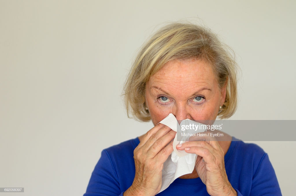 Portrait Of Senior Woman Sneezing Against White Background High