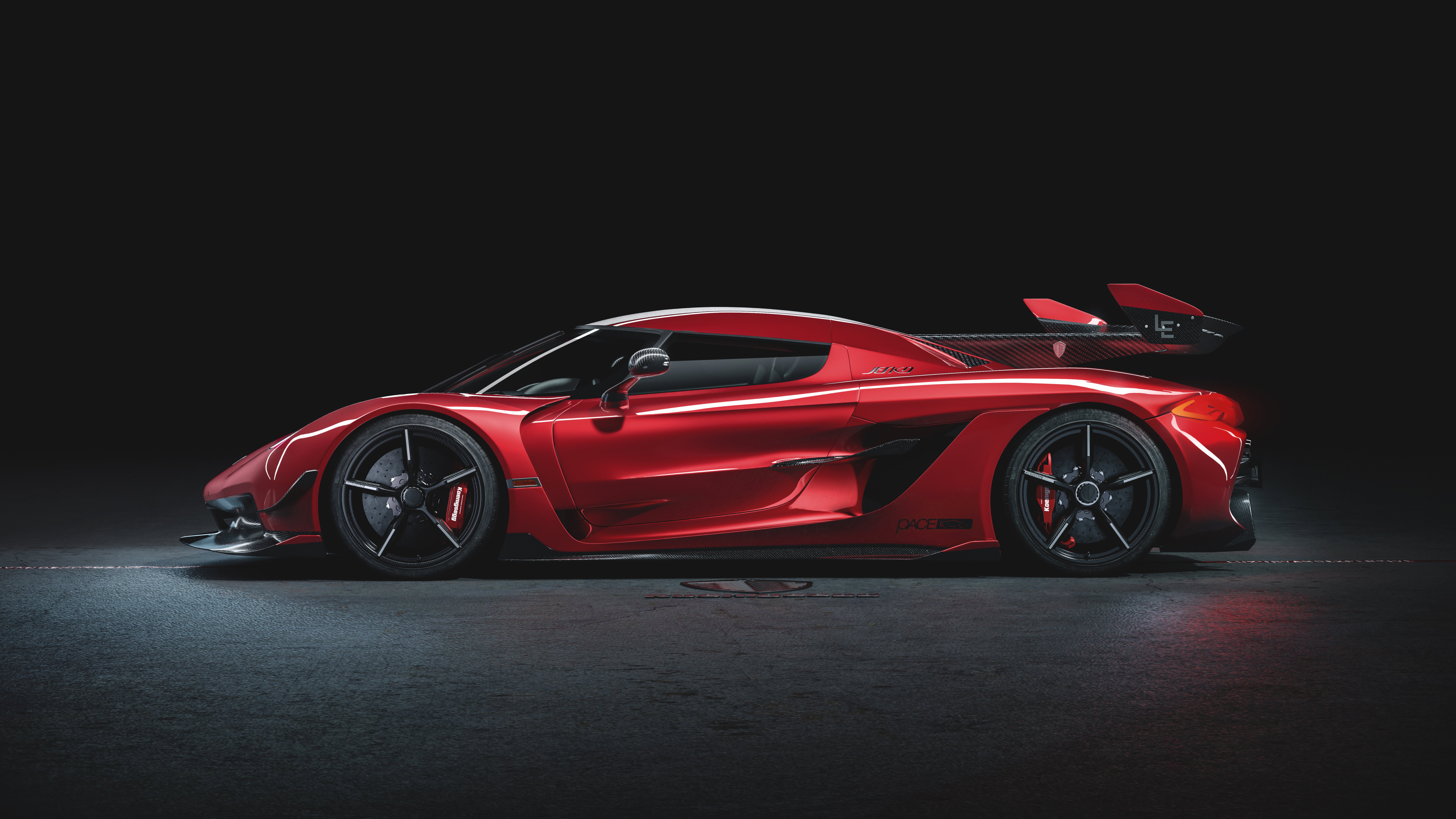 A sleek, red Koenigsegg Jesko sports car, viewed from the side, against a dark background. The car's aerodynamic design and aggressive stance are highlighted