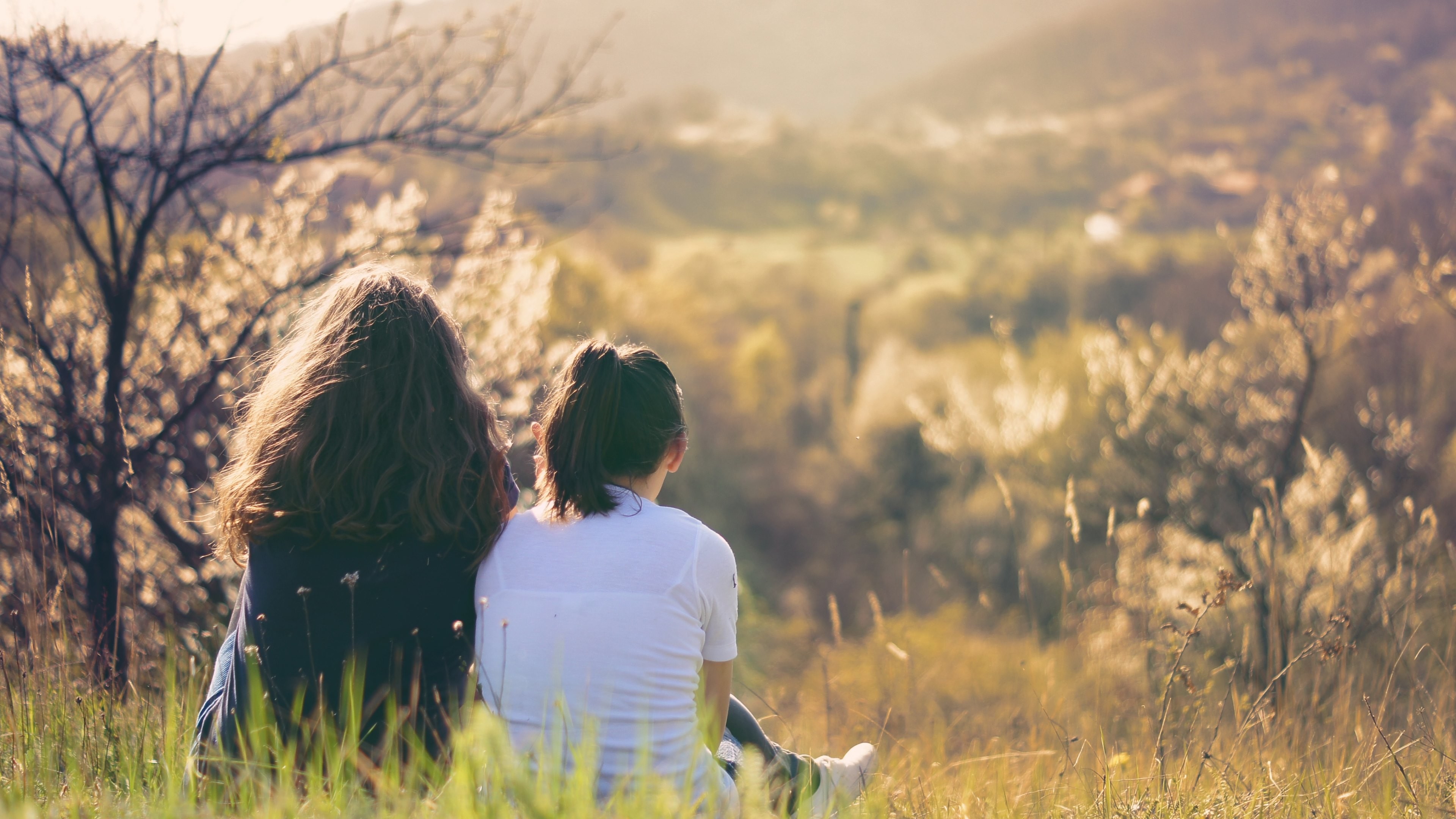 Two friends sit together in a field, enjoying the peaceful view of a valley bathed in the warm glow of sunset. This image evokes a sense of companionship, tranquility, and appreciation for nature