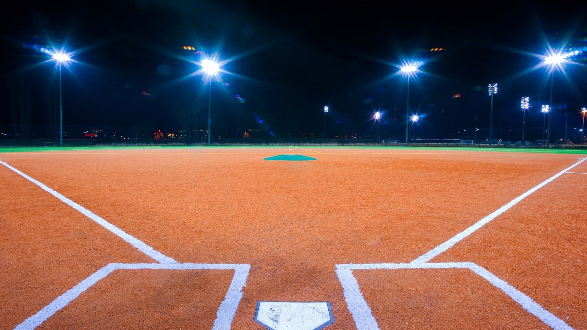 Empty baseball field at night, illuminated by bright lights