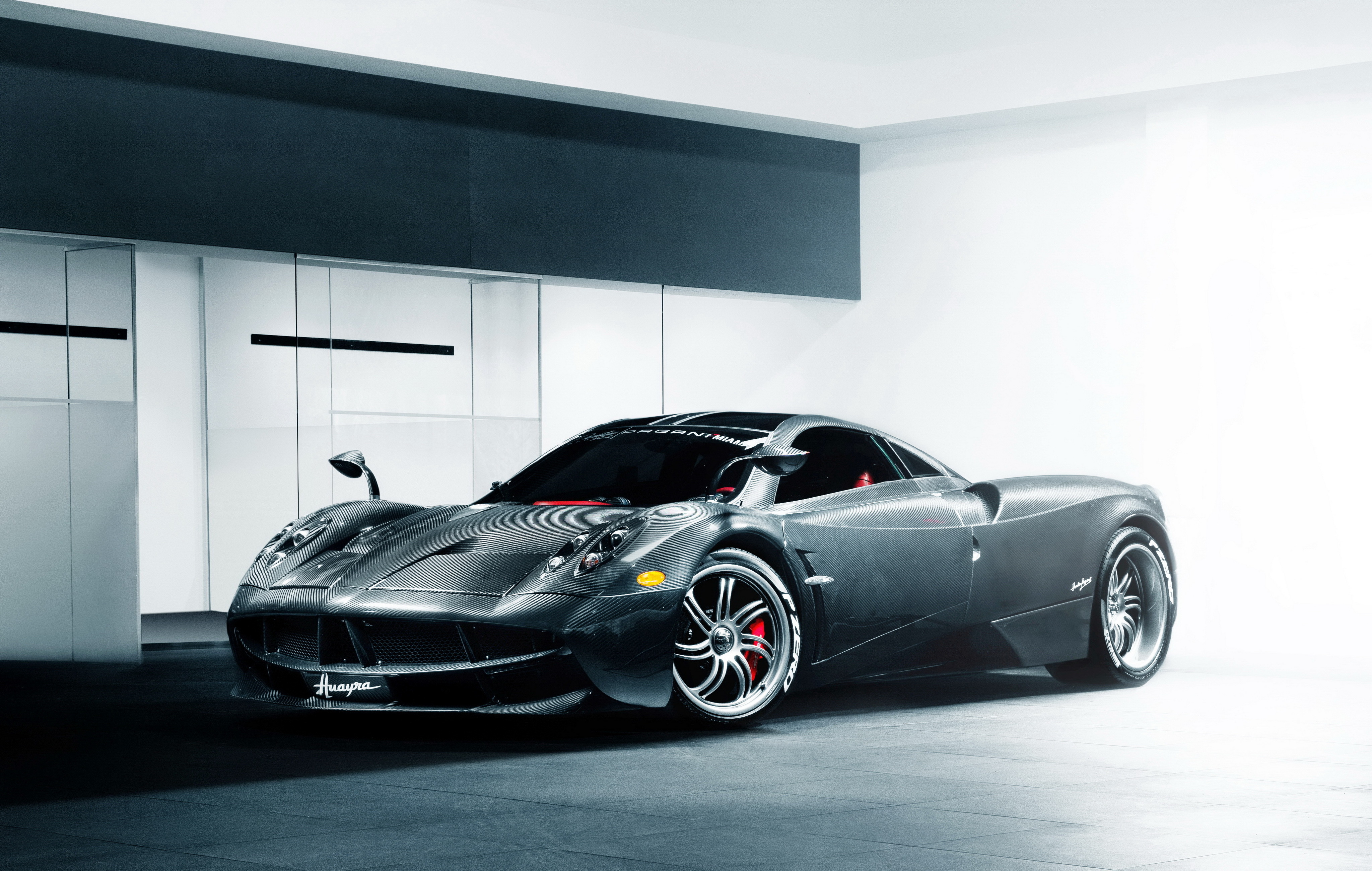 A sleek, black Pagani Huayra supercar with visible carbon fiber bodywork, parked in a modern, minimalist garage