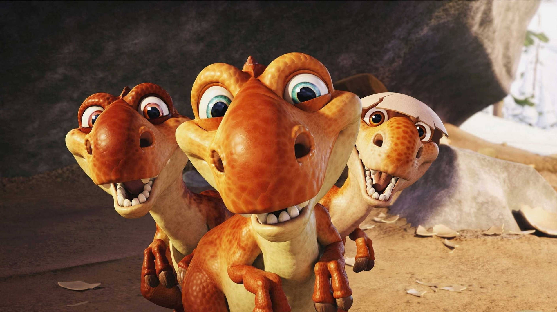 Three adorable animated baby dinosaurs, one still partially in its eggshell, looking at the viewer with wide, curious eyes. The dinosaurs are a warm orange-brown color, set against a blurred background hinting at a prehistoric environment