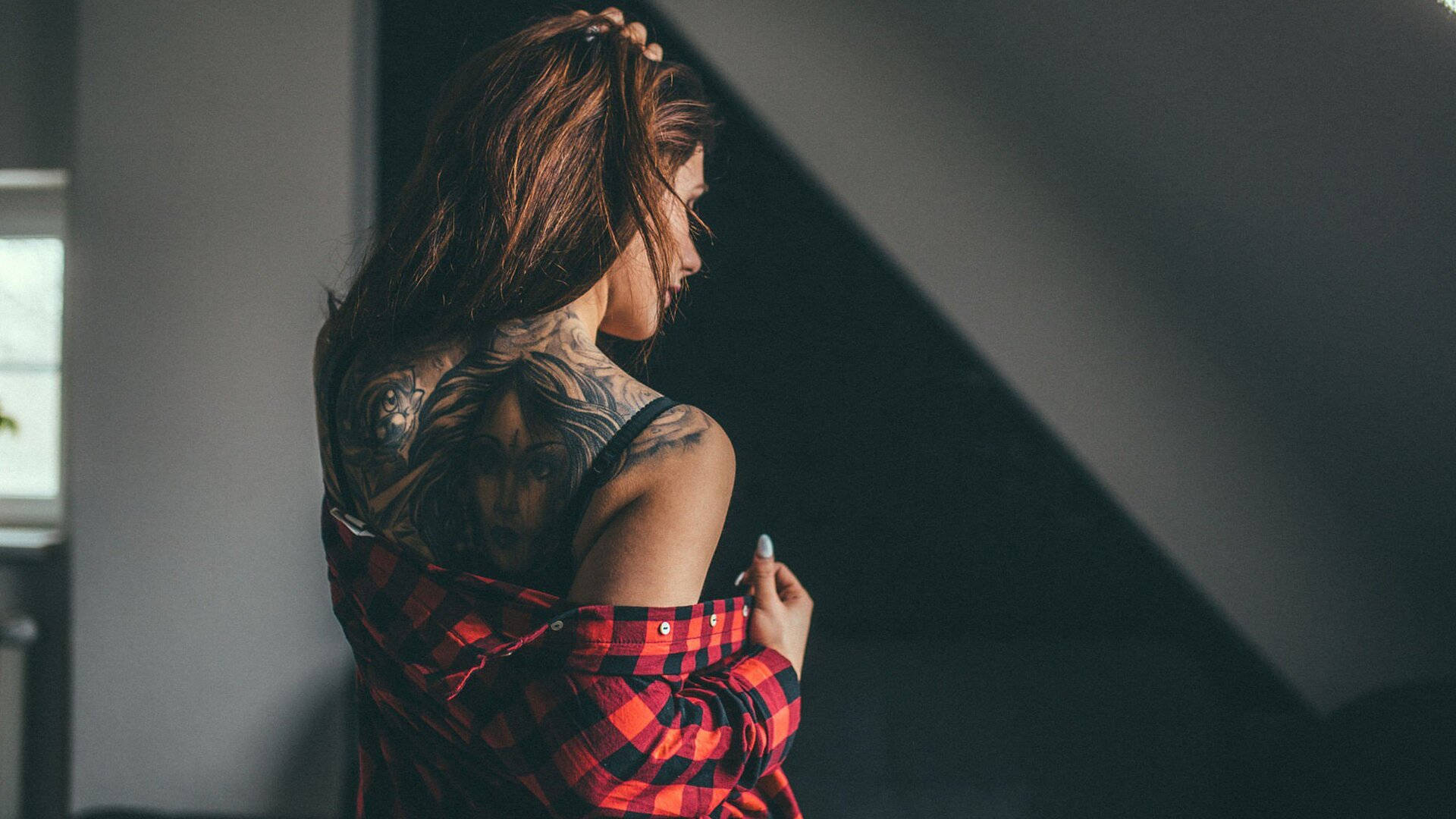 Woman with intricate back tattoo, wearing a red plaid shirt