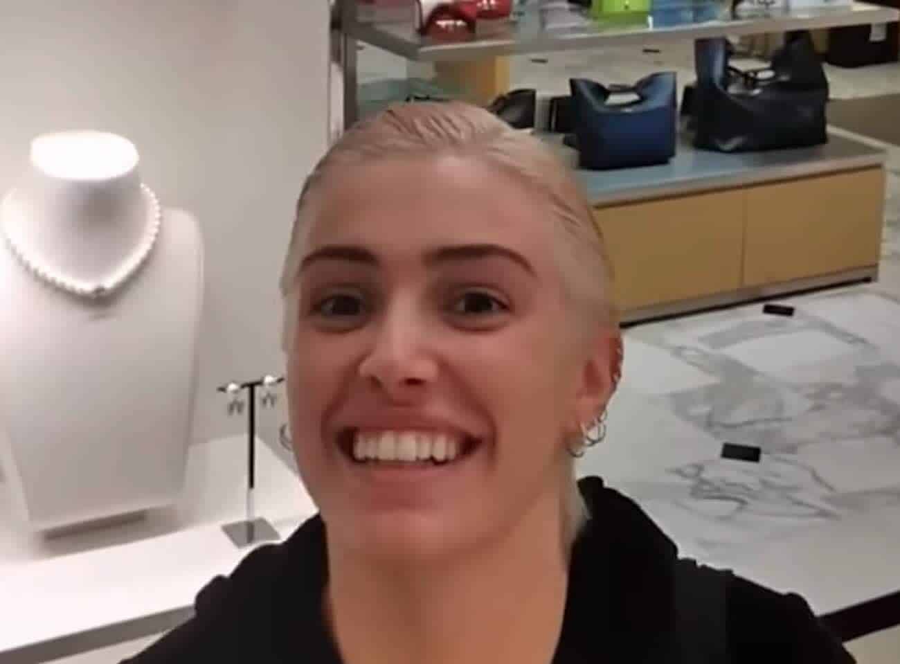 A blonde woman smiles at the camera in a jewelry store. Display cases of jewelry are visible in the background