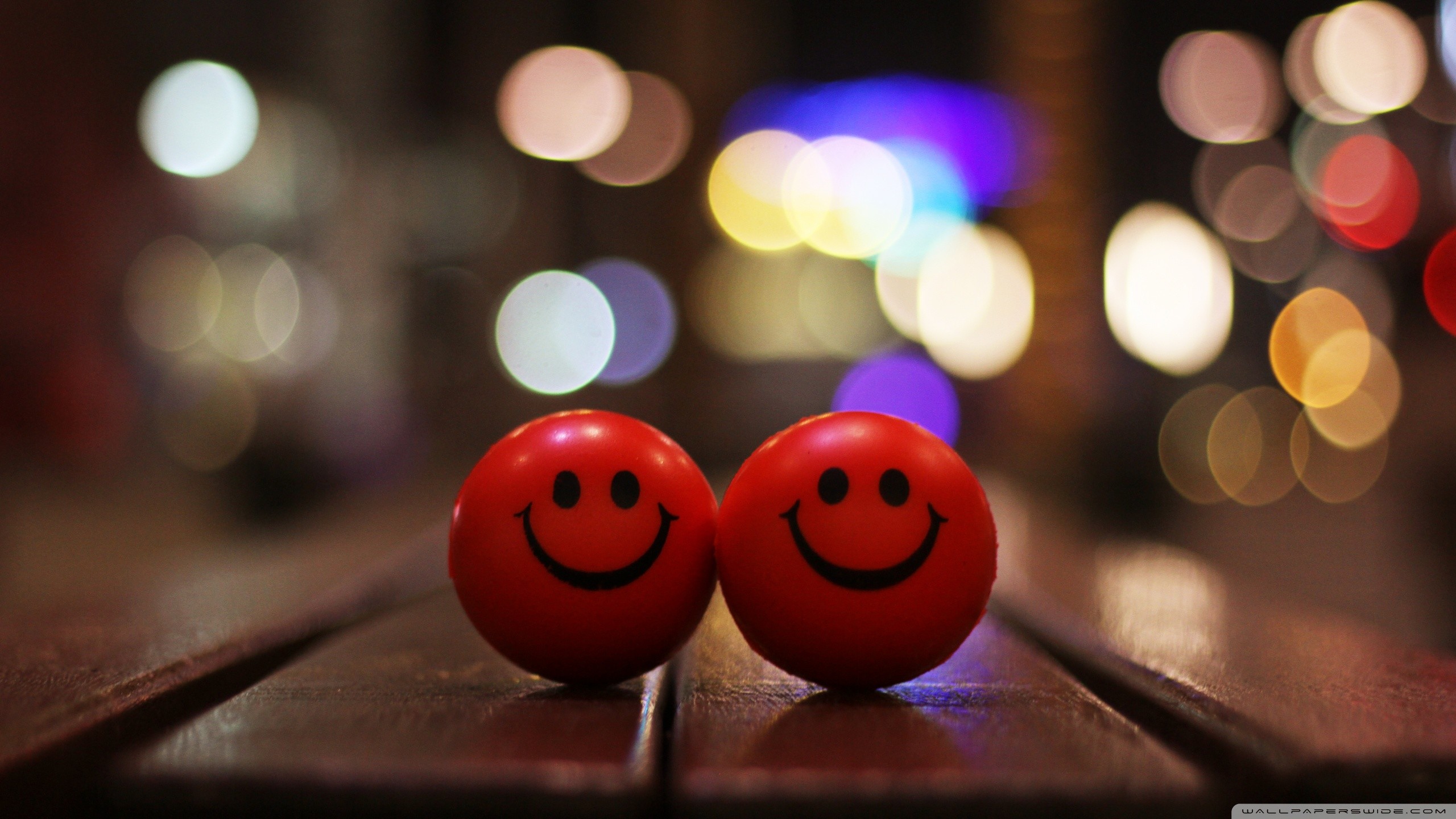 Two red smiley face balls on a wooden surface with bokeh lights in the background