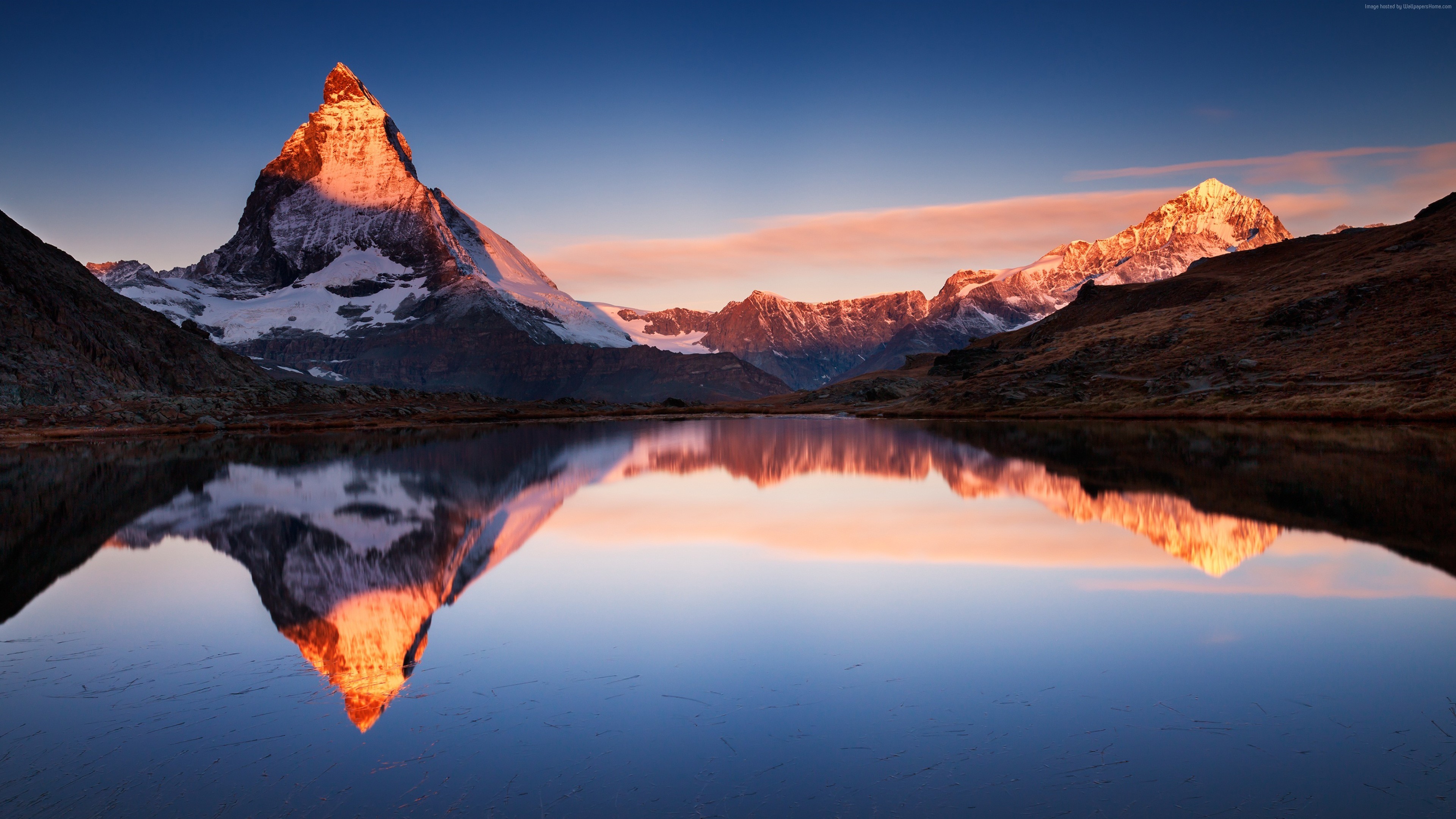 4K wallpaper of Matterhorn reflecting in Stellisee lake at sunset with Matterhorn's orange peaks, pink clouds, and blue sky