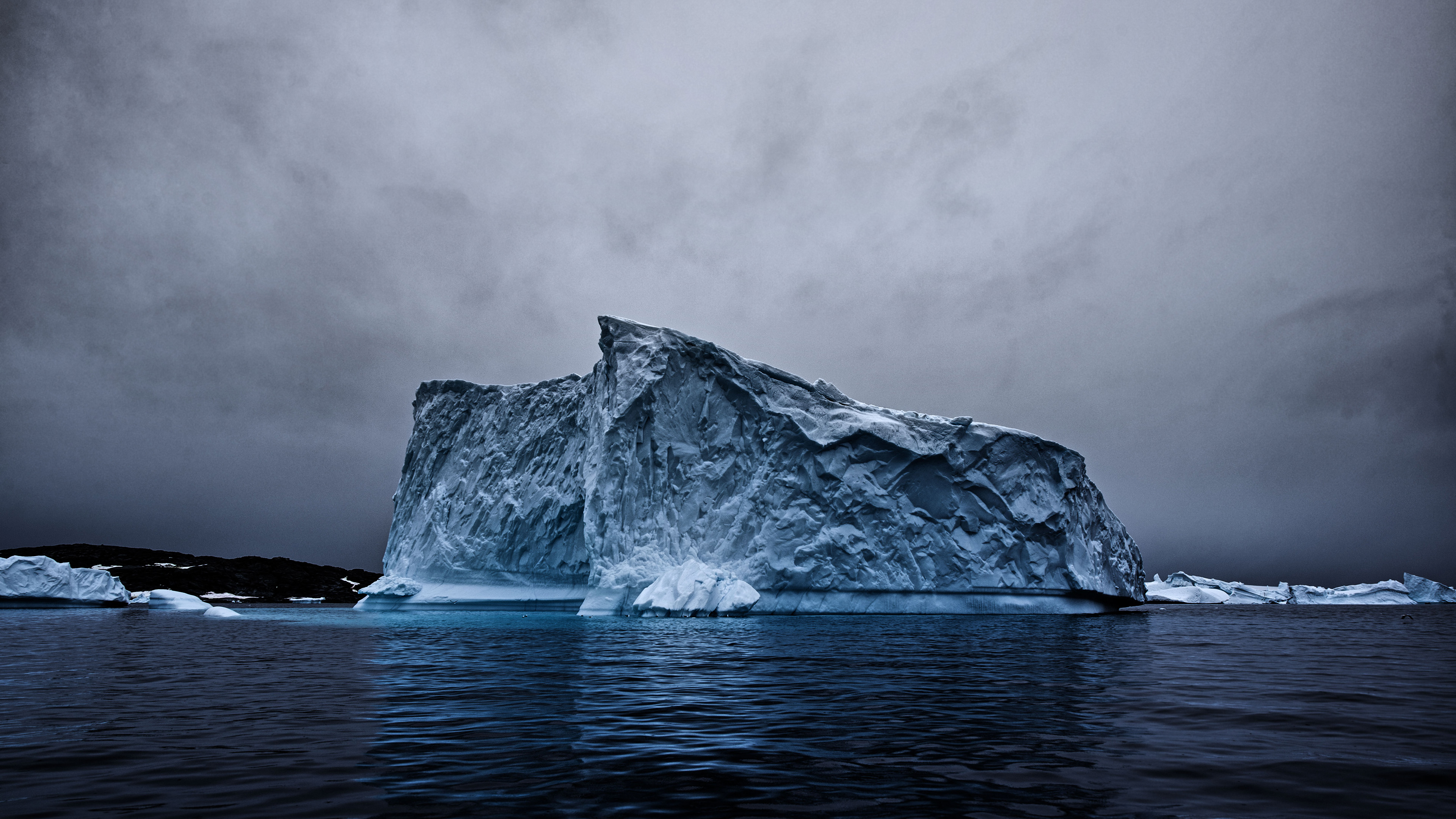 A majestic iceberg floats in dark, icy waters under a cloudy sky