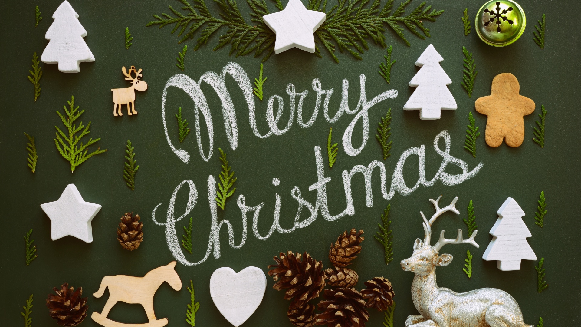 Festive flat lay of Christmas decorations on a dark green background with the chalk lettering 'Merry Christmas'