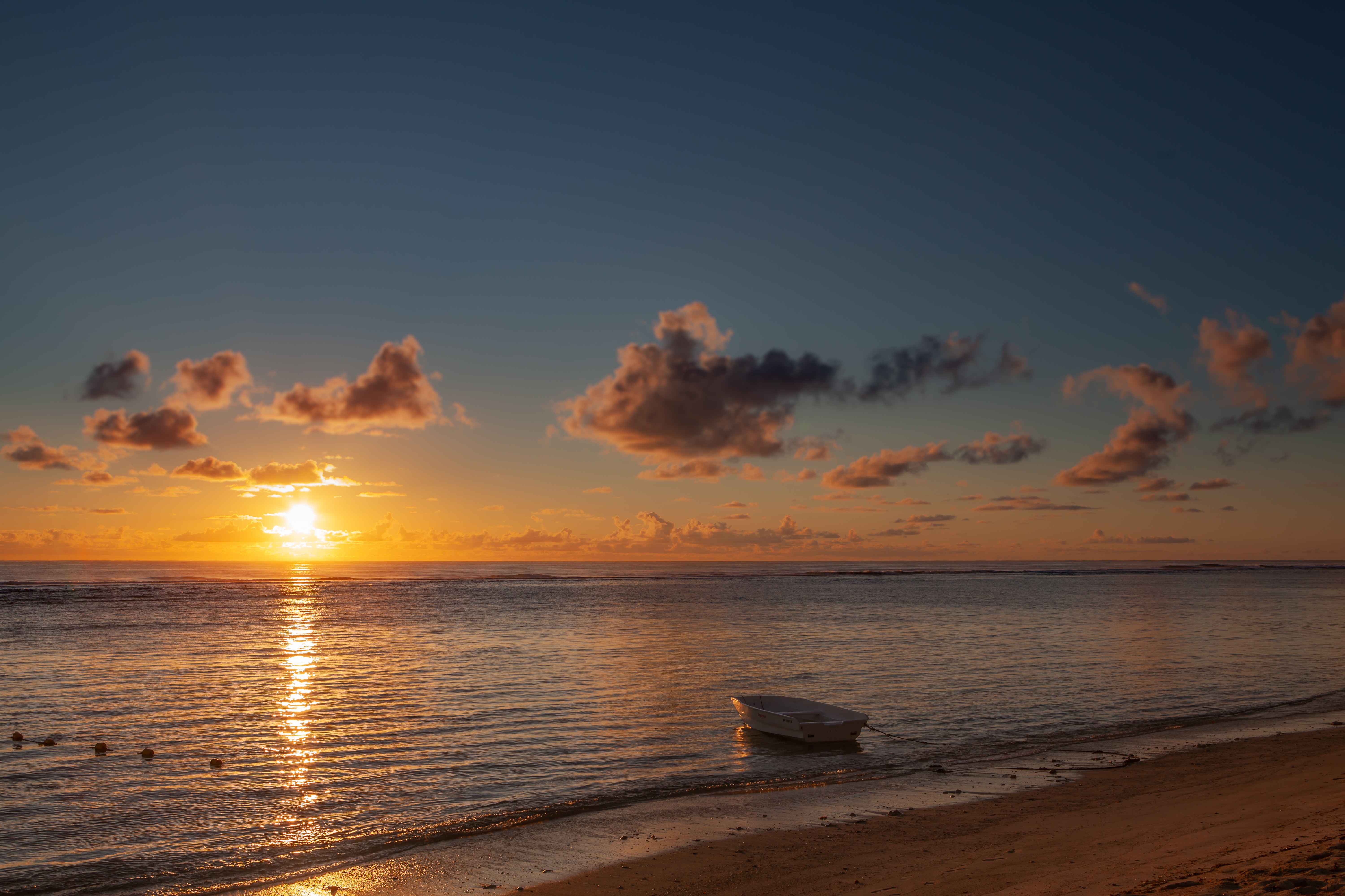 A serene sunset over a calm ocean with a small boat moored near the shore, perfect for a sea wallpaper