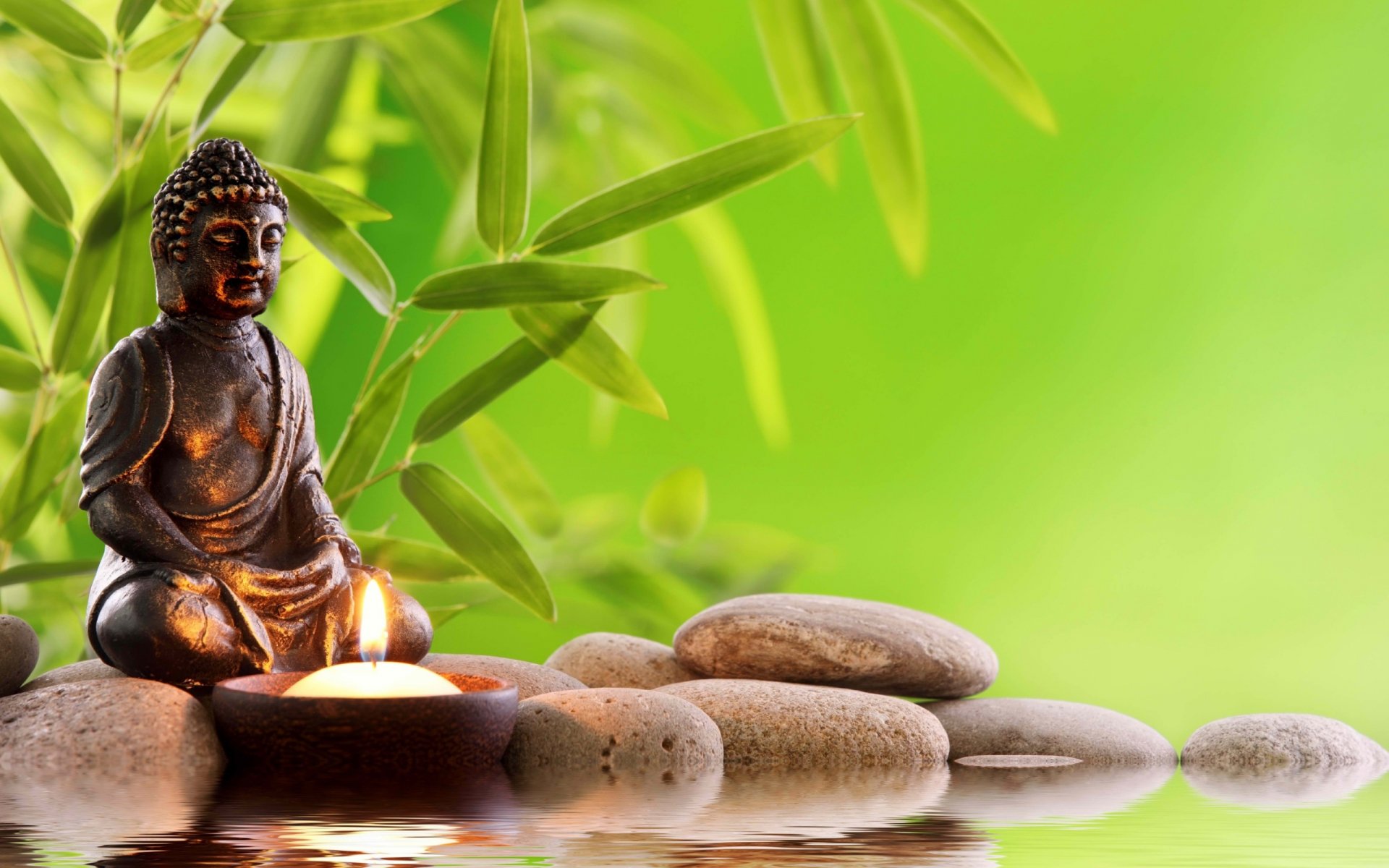 Serene Buddha statue with a lit candle amidst bamboo and stones reflected in water
