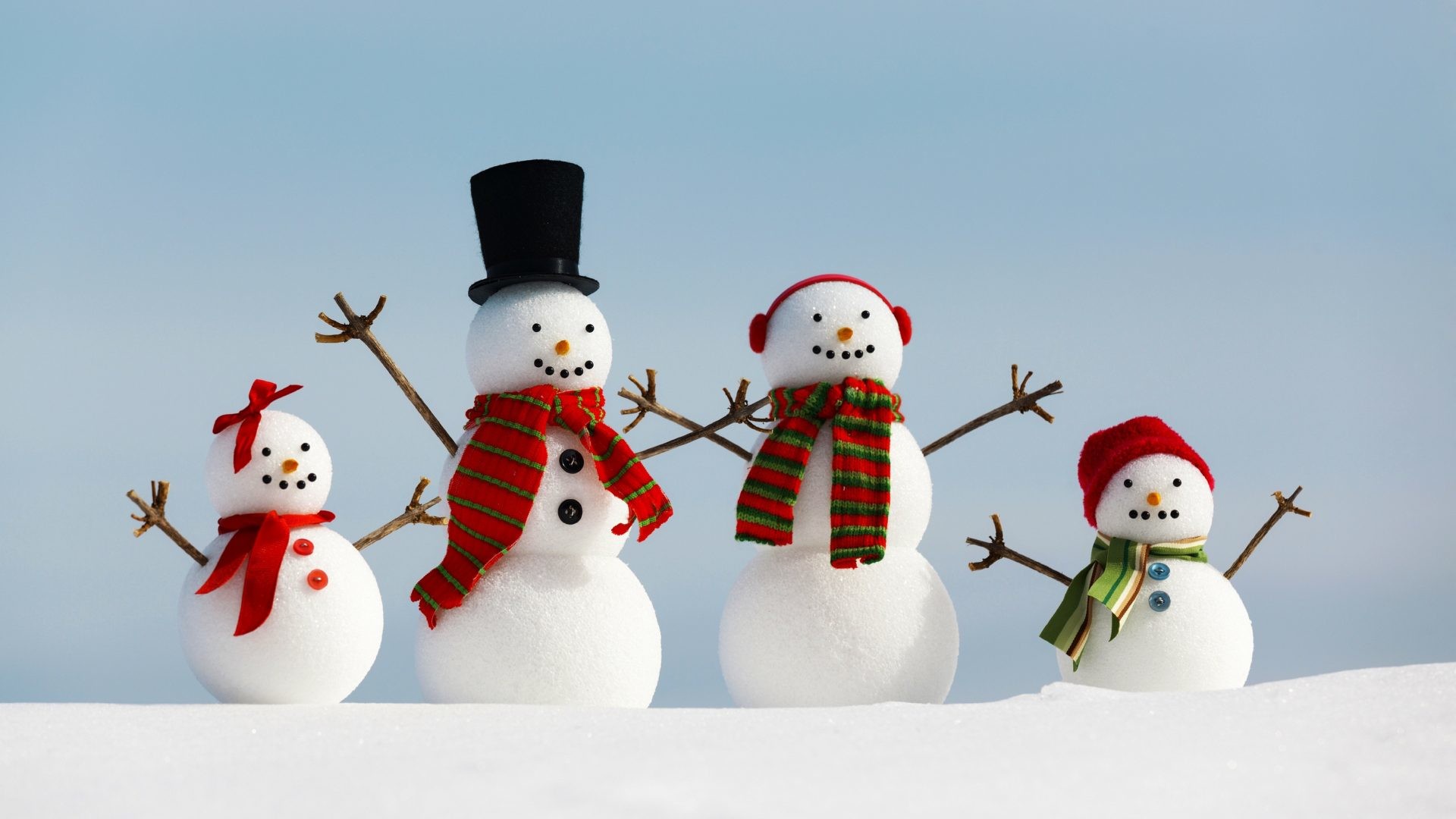 Four adorable snowmen dressed in festive scarves and hats stand in the snow against a clear blue sky