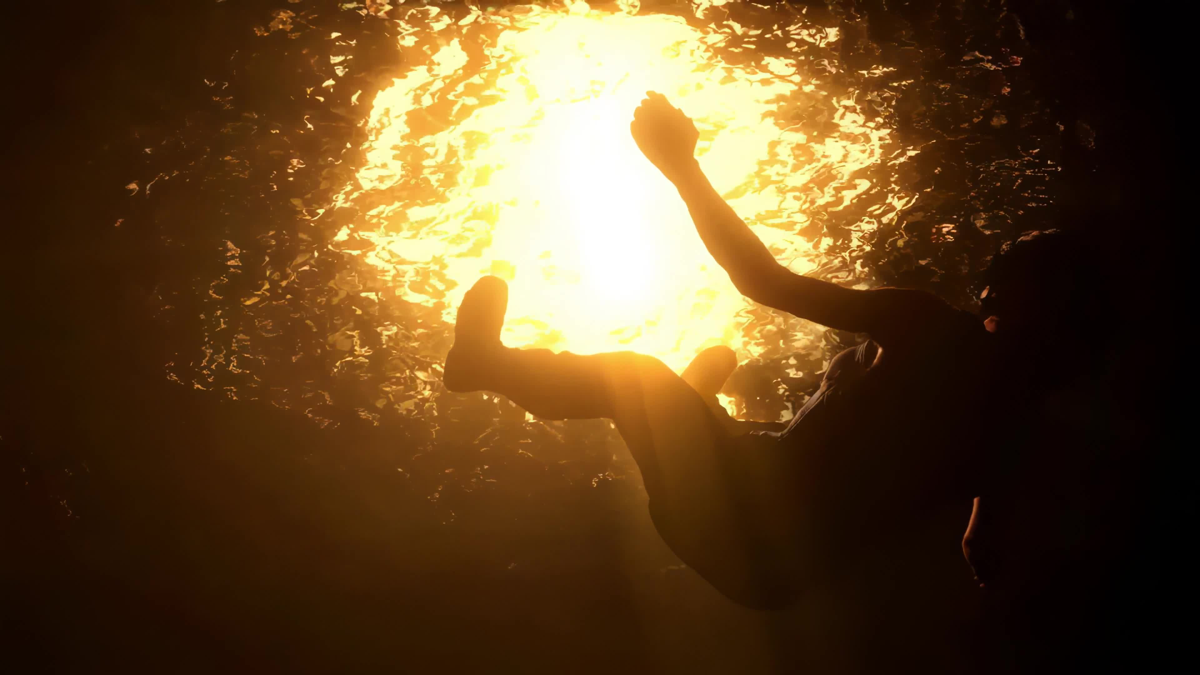 Silhouette of a person reaching for the light filtering through water in a dark cave