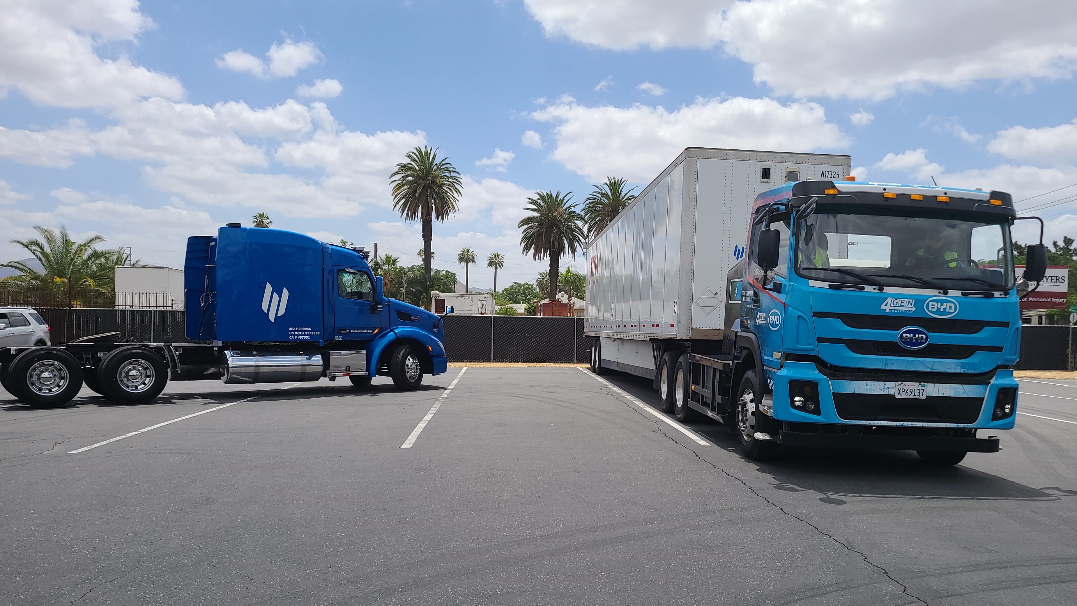 Two BYD electric semi-trucks, one with a trailer, parked in a parking lot
