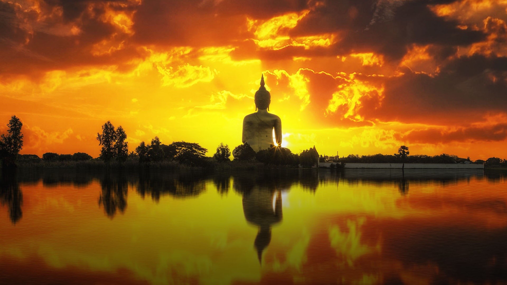 Serene Buddha statue silhouetted against a vibrant sunset reflected in calm water