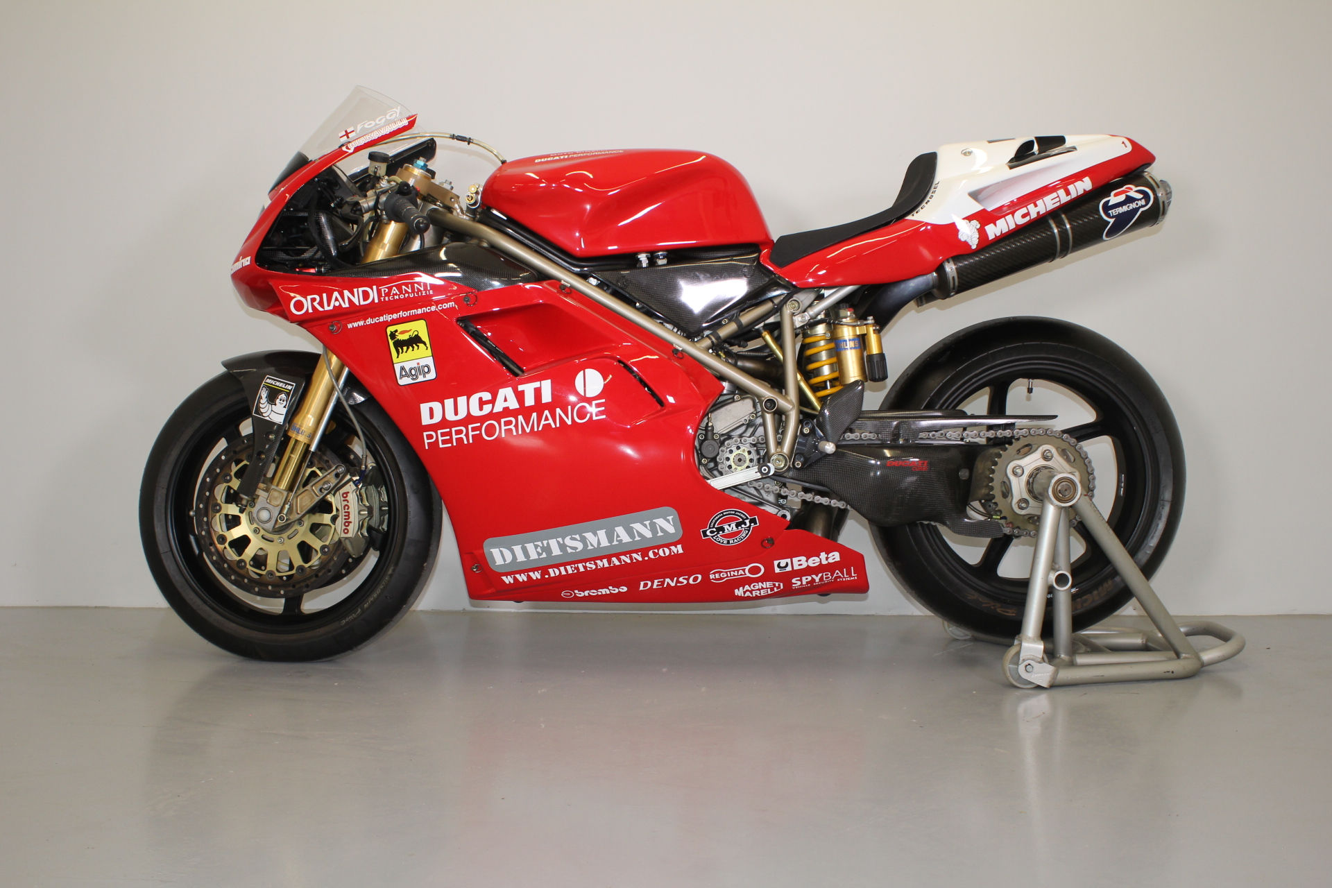 A Ducati 996 racing motorcycle in red and white livery, displayed on a paddock stand