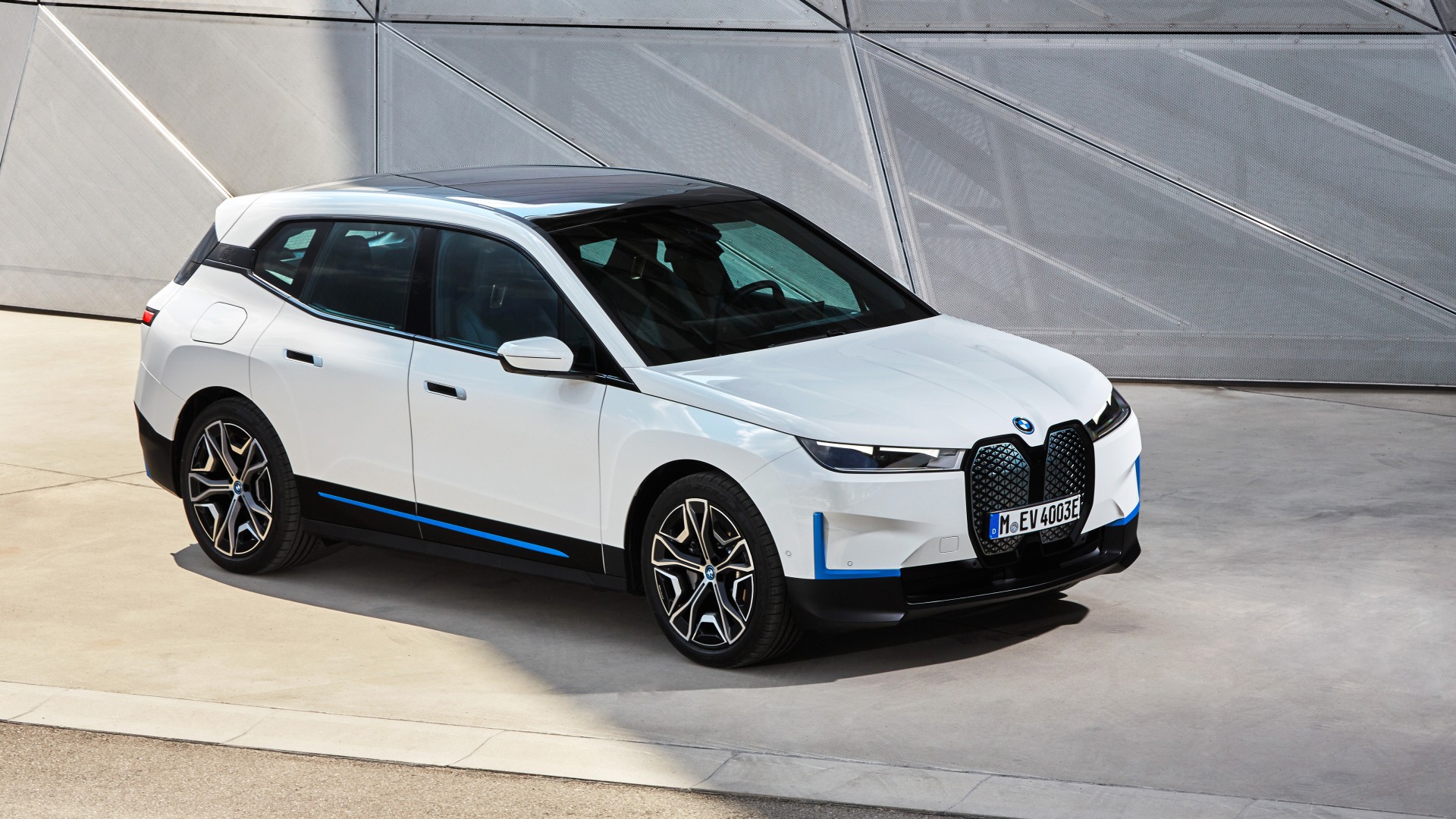 A white BMW iX electric SUV parked in front of a modern, angular building