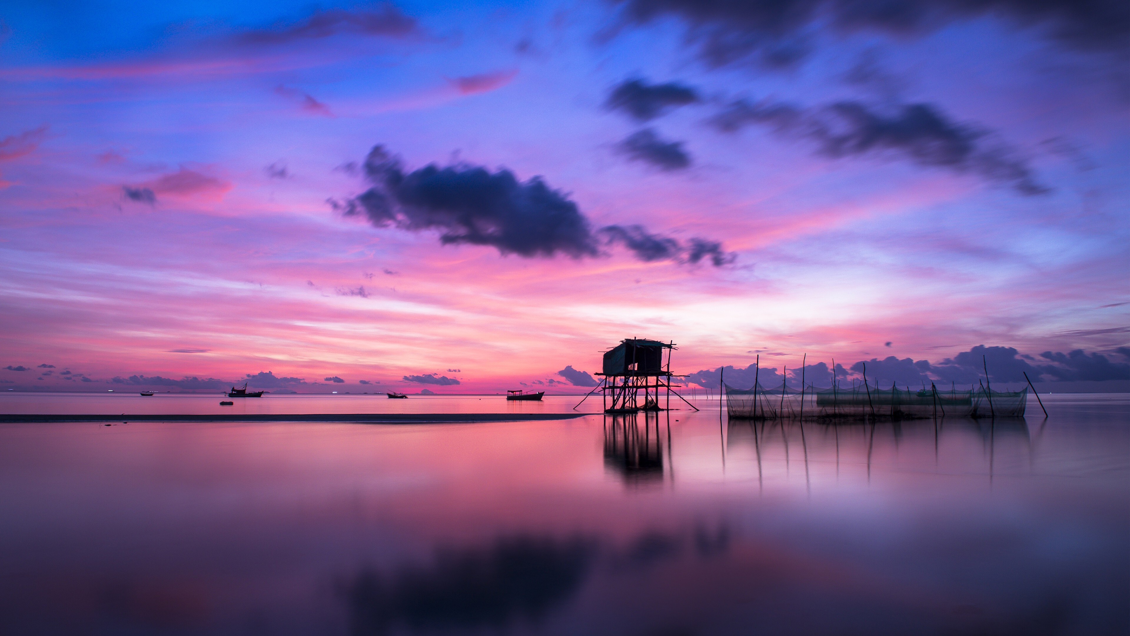 A serene island sunset with traditional fishing hut and boats, reflecting in the calm water