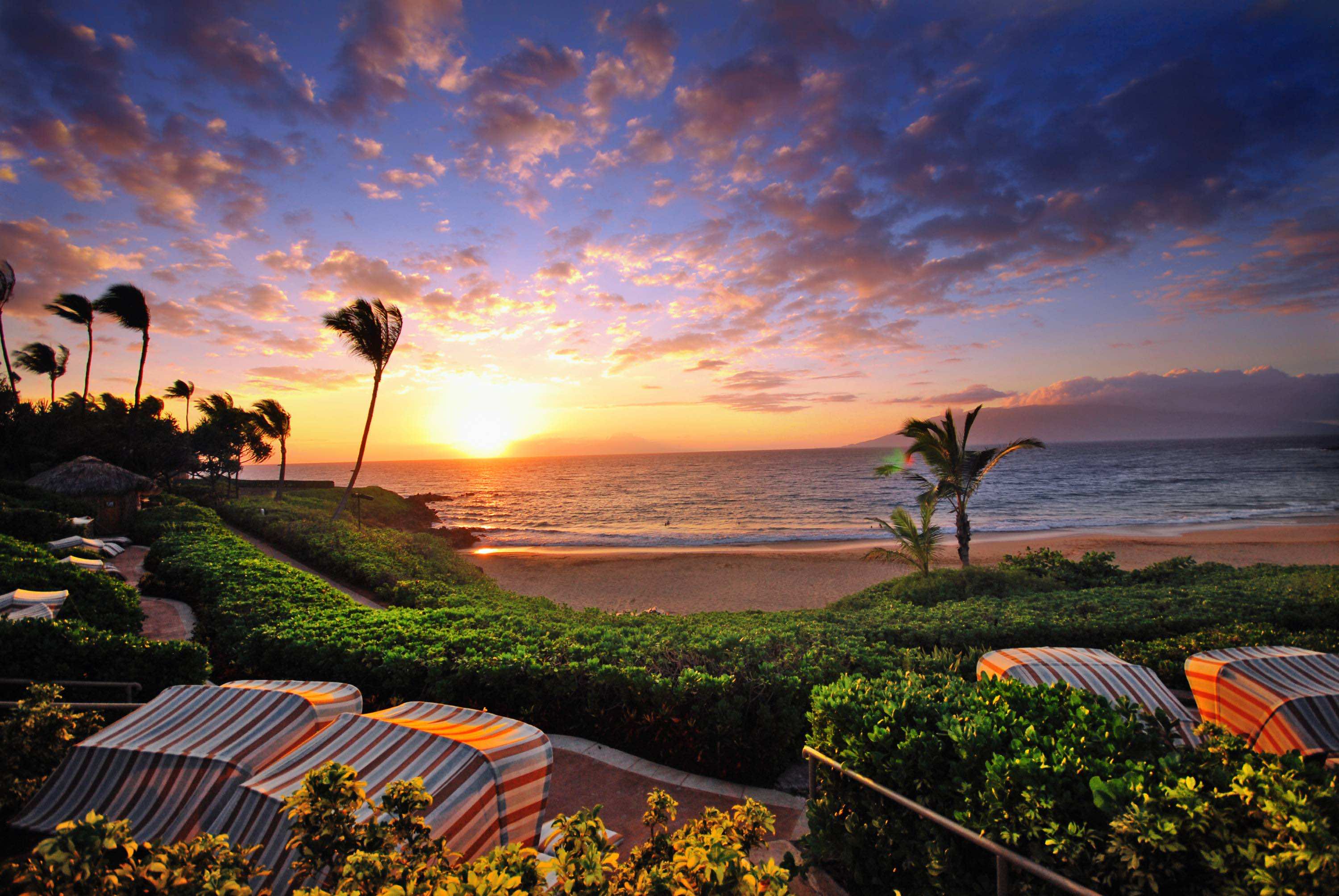 A breathtaking Hawaiian sunset over the Pacific Ocean, with palm trees swaying in the gentle breeze and beach cabanas inviting relaxation